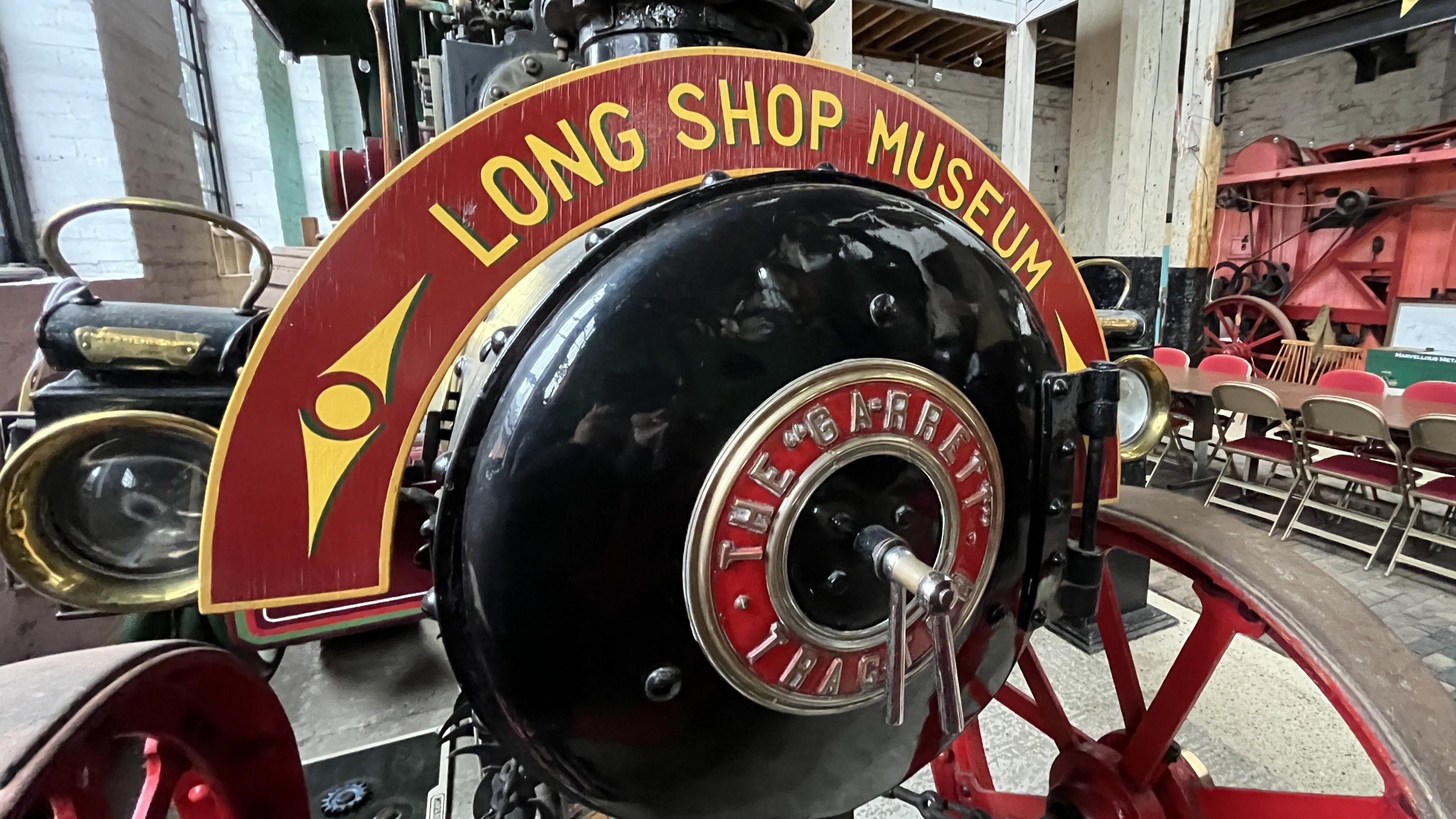 An old piece of steam engine equipment sits in a museum. It is black and red and has the name of the museum painted on it.