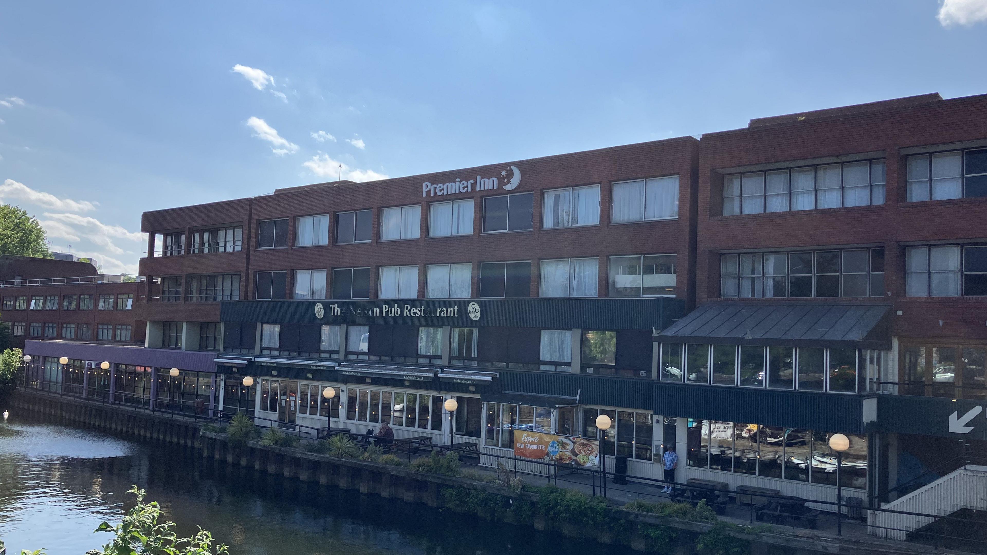 A riverside hotel and restaurant is pictured with a river in the foreground