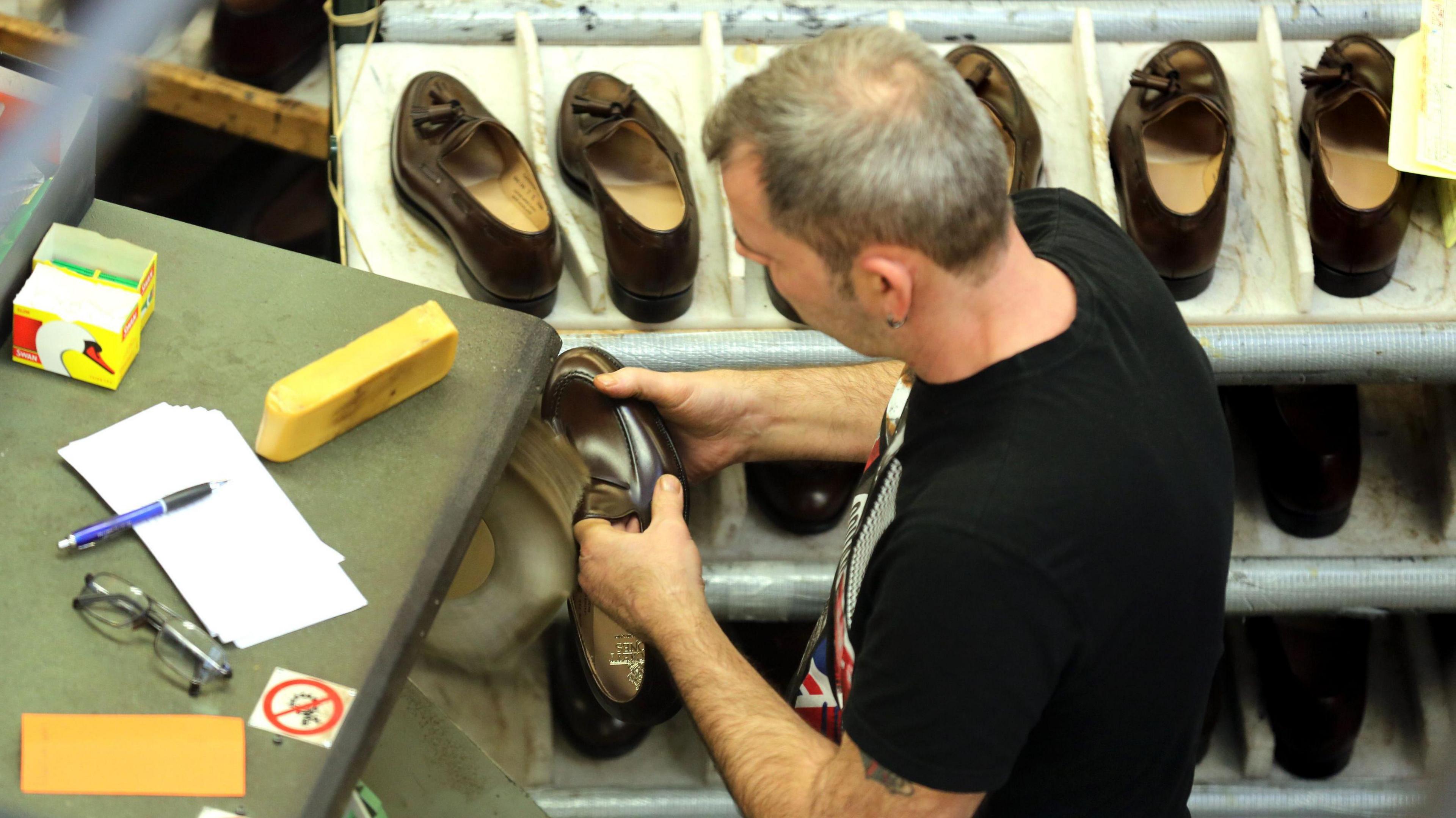 Man buffing a new shoe in a factory as a selection are on show on a table in front of him