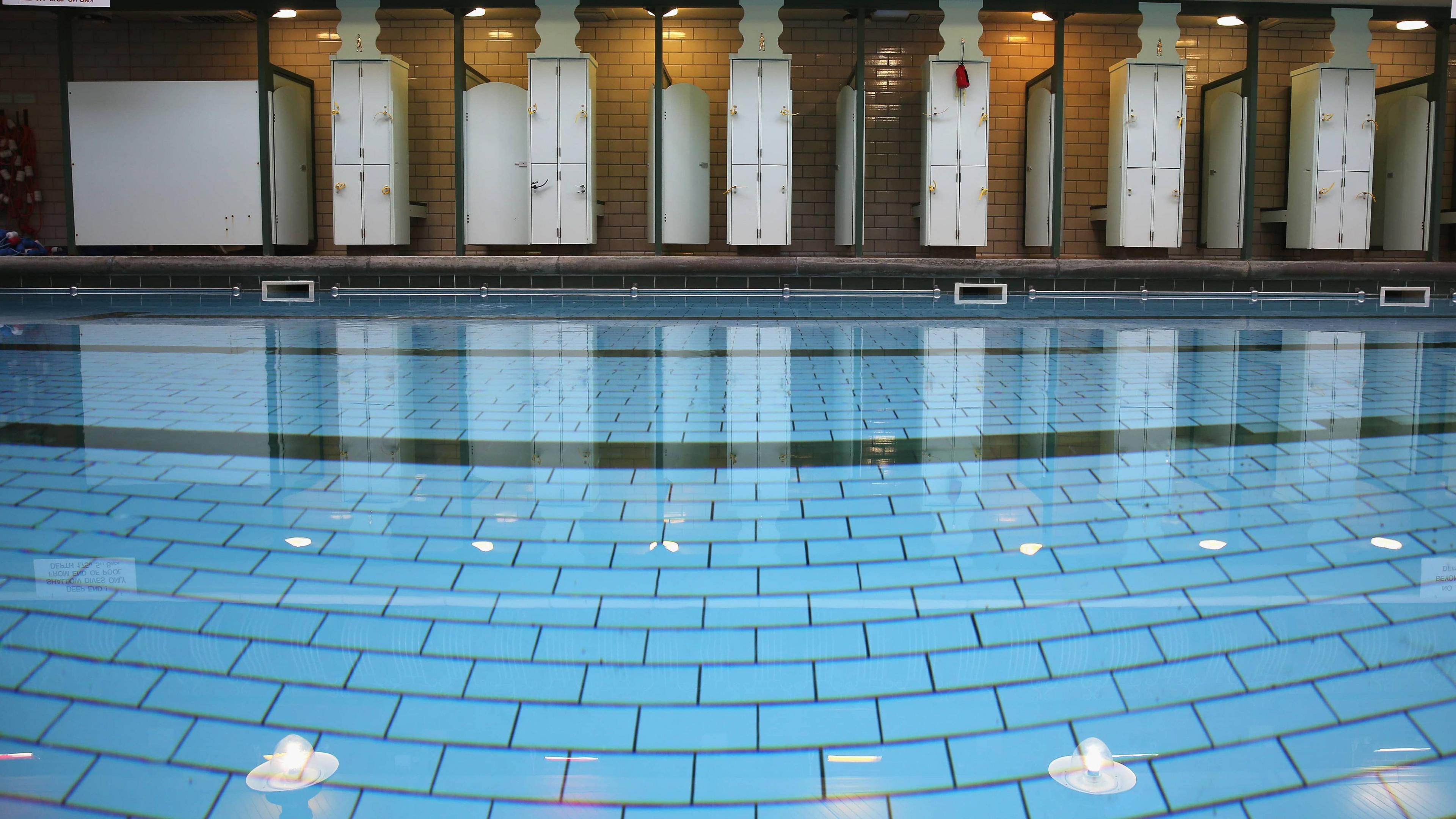 An empty well-lit swimming pool, with changing rooms running along the poolside.