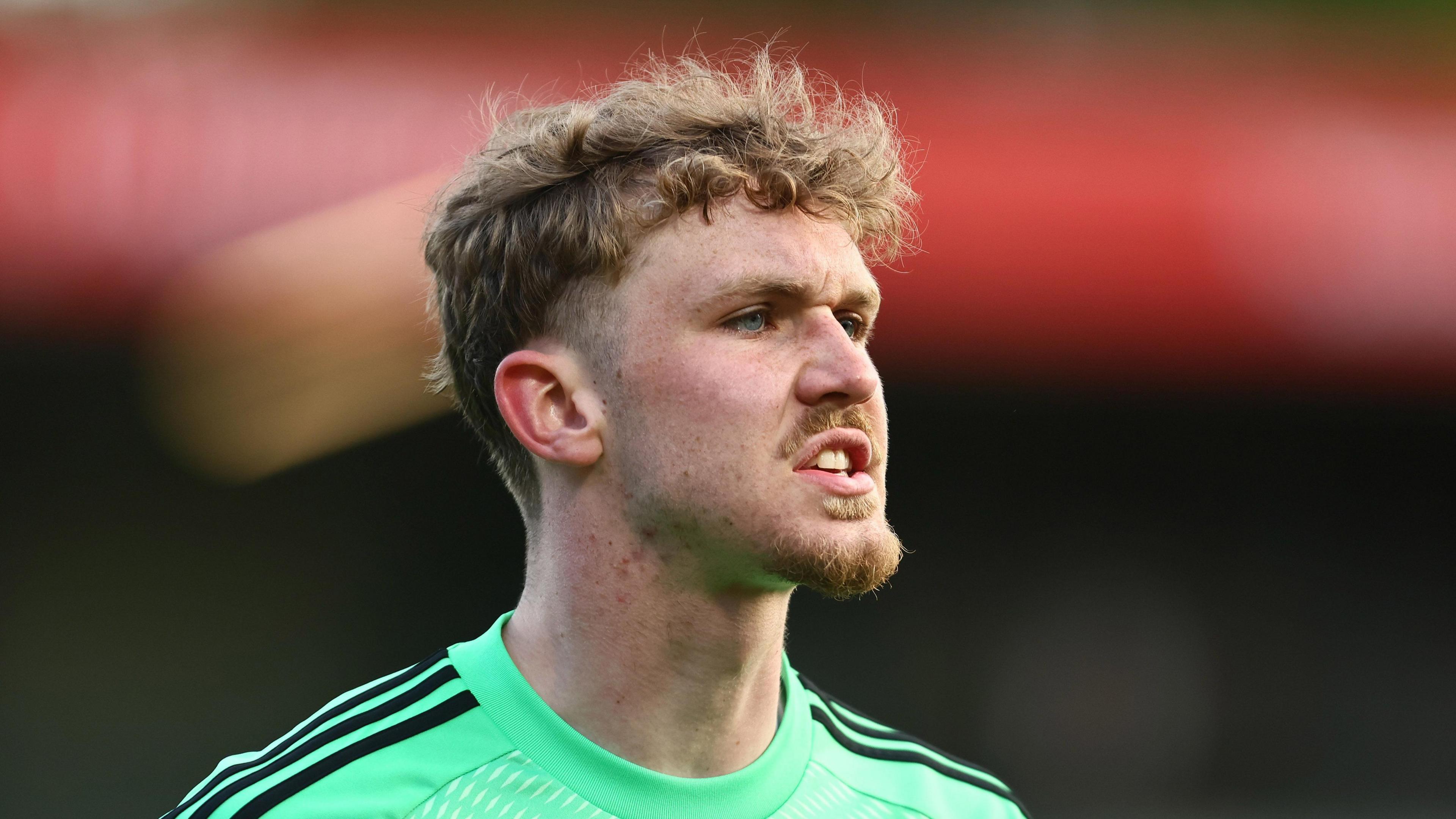 Matty Young playing for Salford City, wearing a lime green goalkeeper top and about to shout something.
