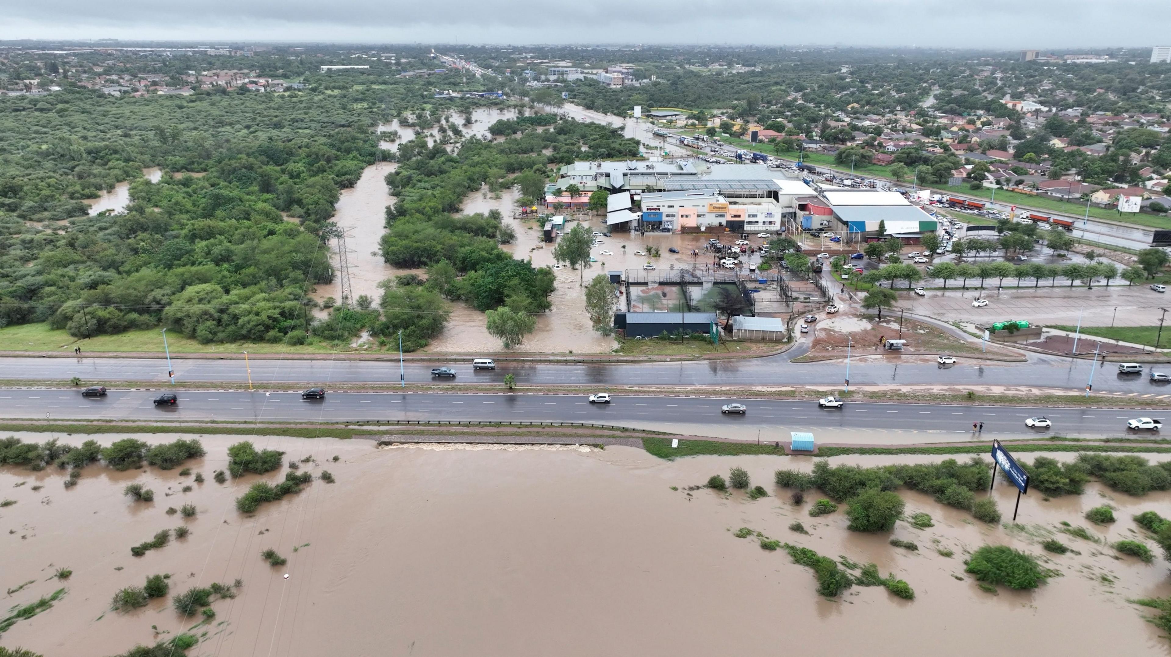 Drone view shows flooded area at Molapo Crossing Mall and the Western Bypass Highway in Gaborone in Botswana with view of dual carriageway with moving vehicles in centre.