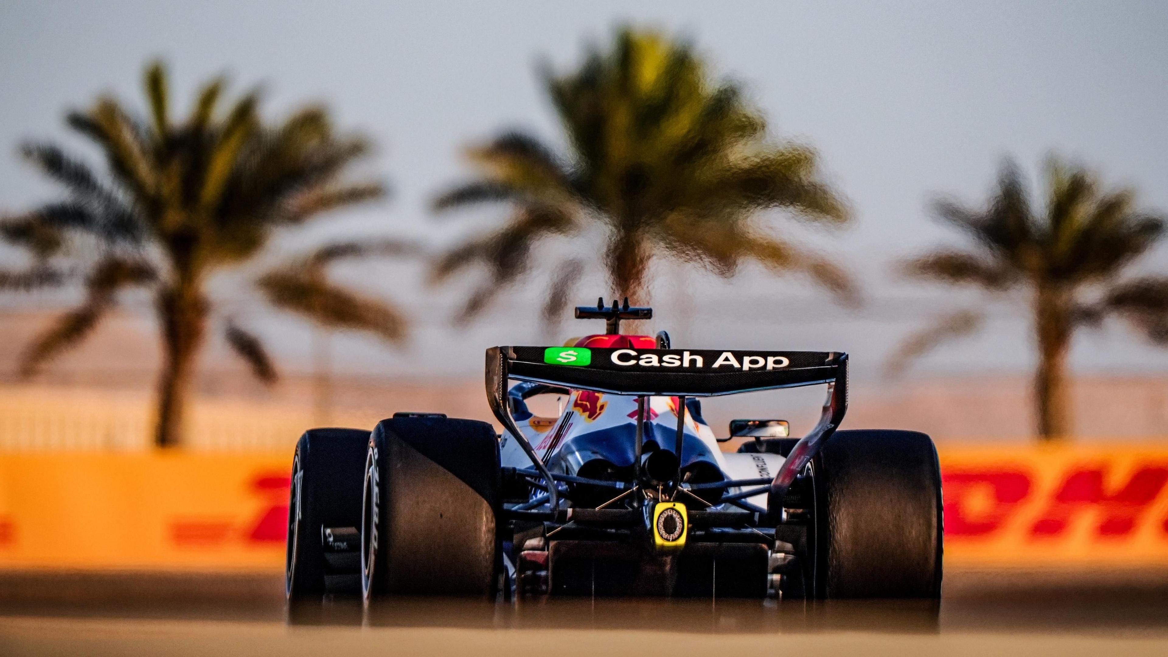 An FI car drives around a race course with palm trees an red and yellow lettering in the background. 