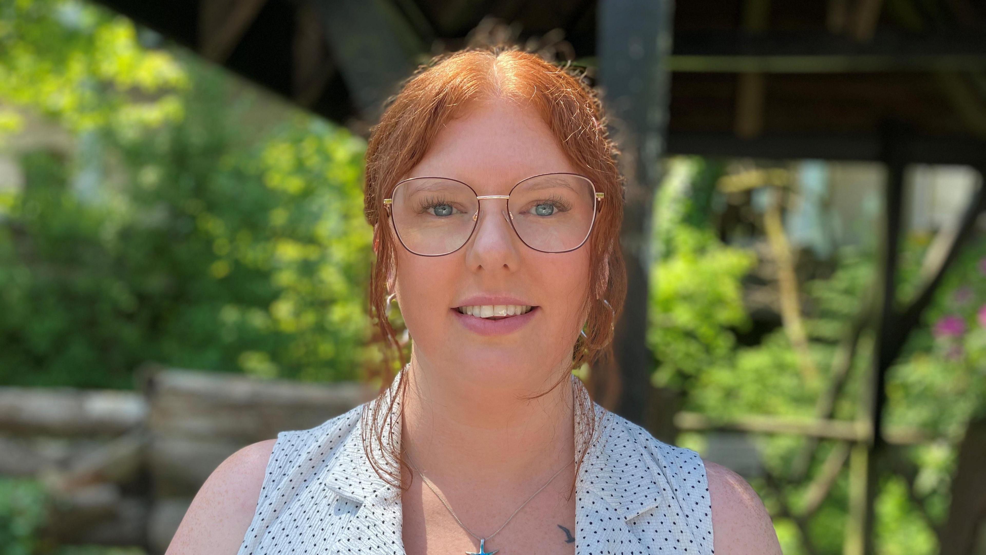 Ellie Robertson, who has red hair tied back, and wearing glasses and smiling at the camera