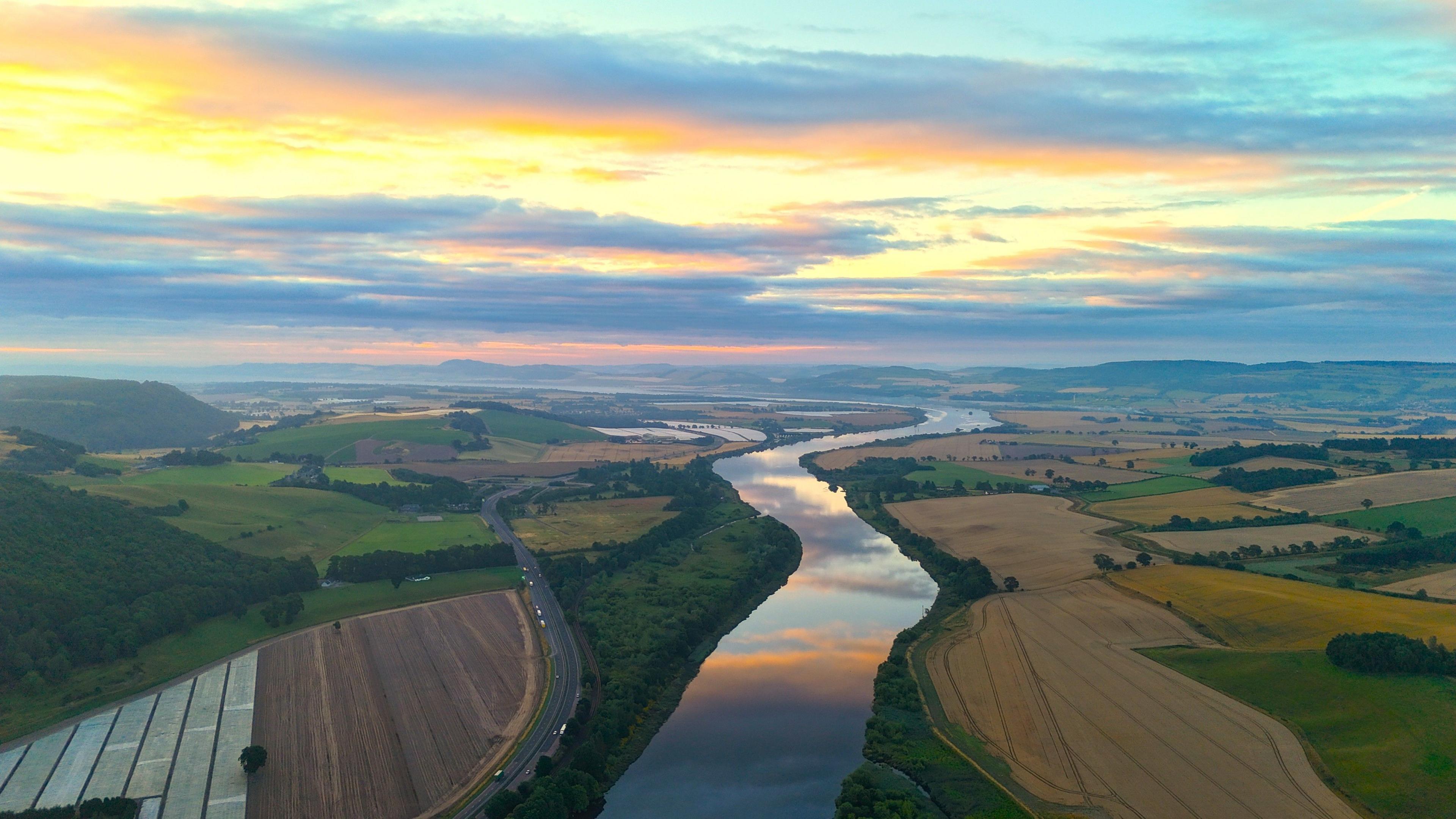 Aerial view of the River Tay, winding between fields on both sides below a vivid blue, yellow, orange and pink sky at sunrise
