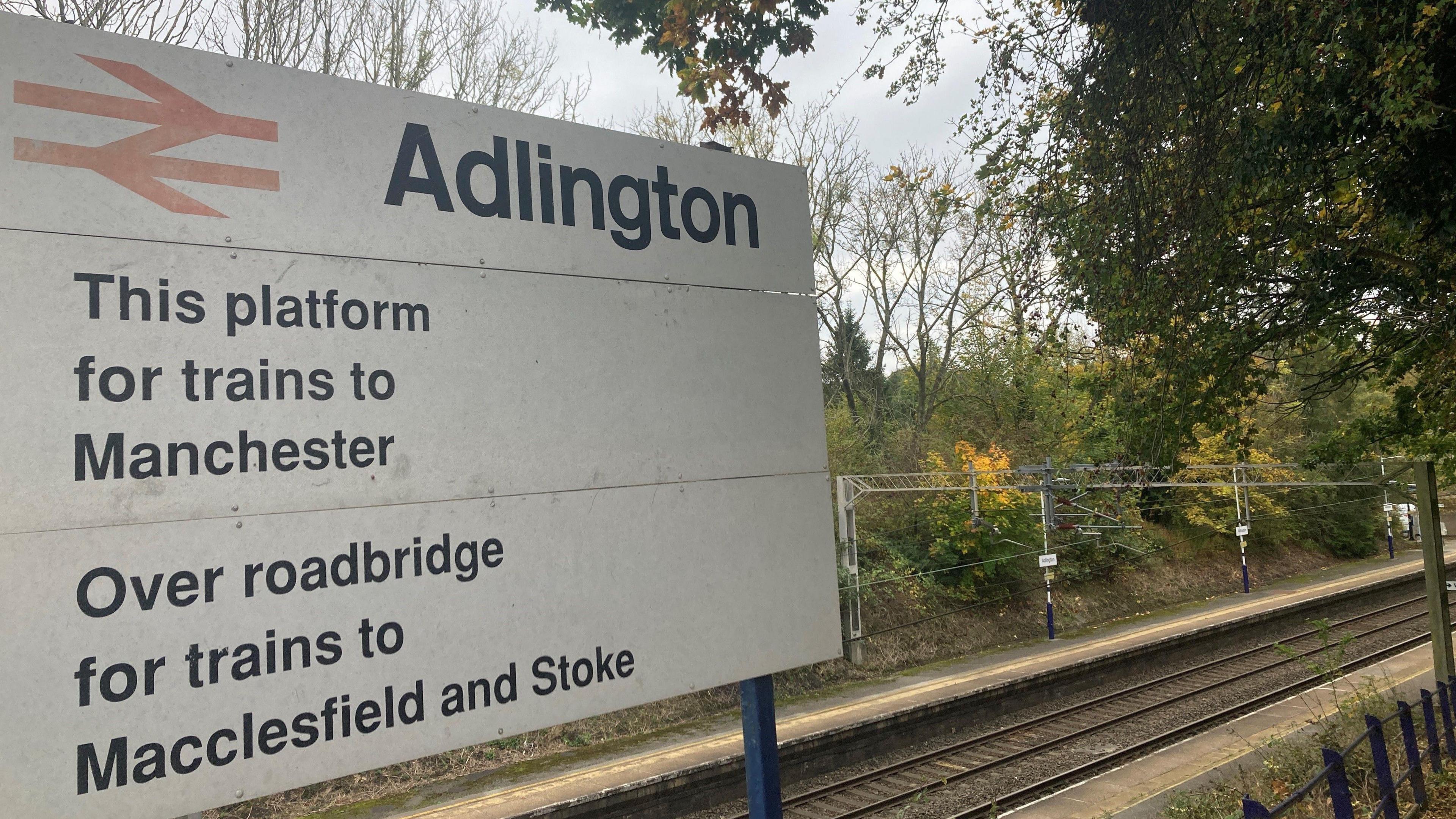 View of the Adlington Railway Station sign. It says "this side for trains to Manchester" and "over roadbridge for trains to Macclesfield and Stoke".