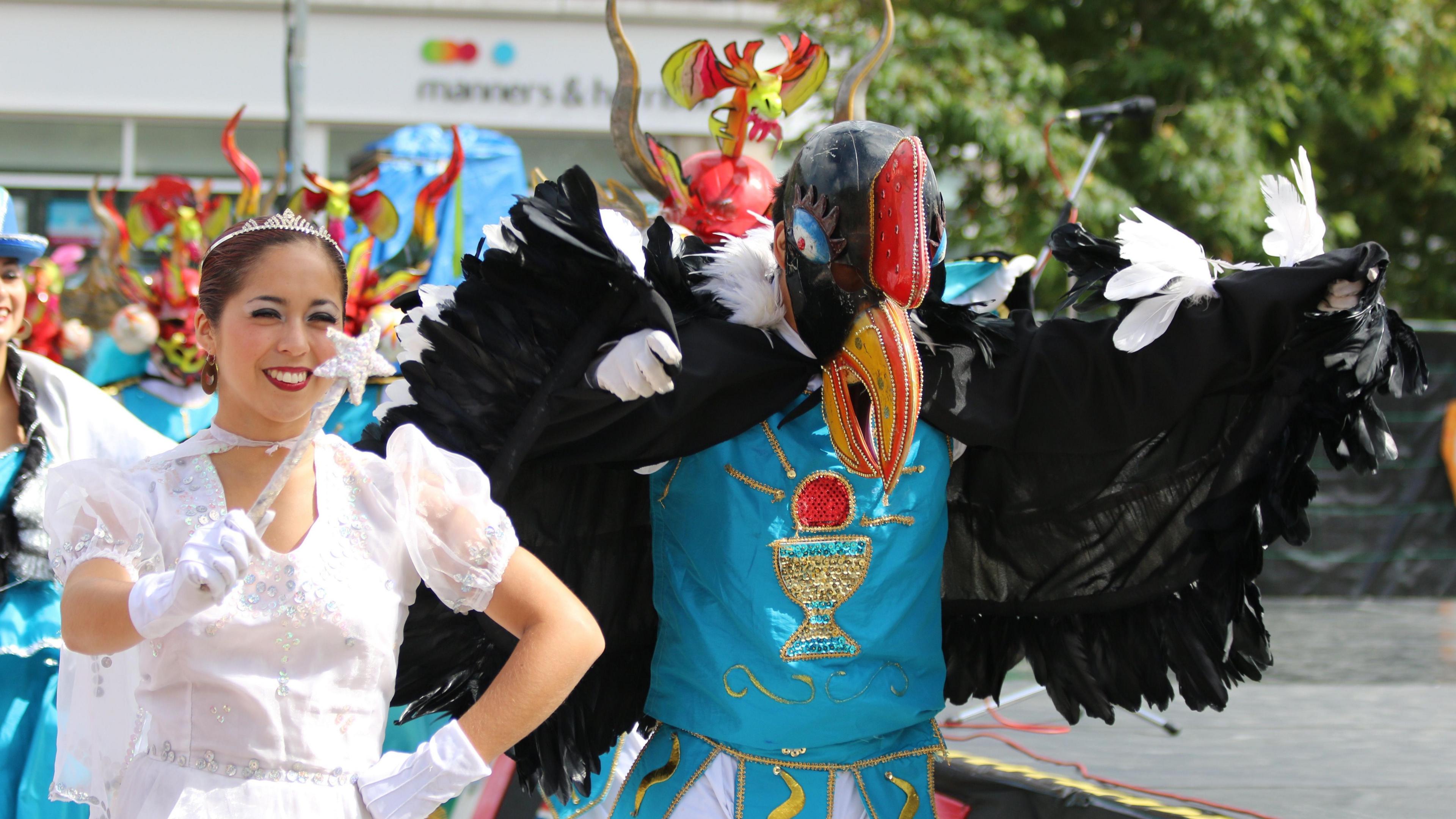 The Ballet Folklorico Tupa Marka from Chile performing at the festival. A woman wearing a white costume, tiara and a star-tipped wand is walking next to a man dressed as a black bird.