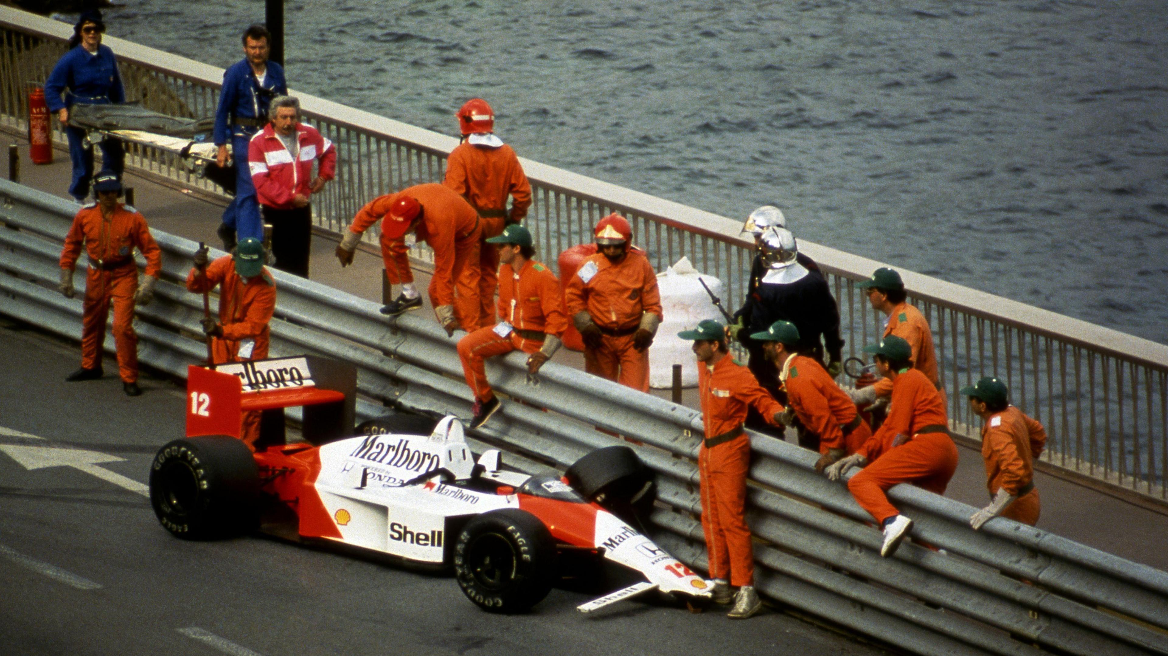 Marshals clamber over the barrier at Portier to attend to the damaged McLaren of Ayrton Senna, who crashed out of the lead in 1988