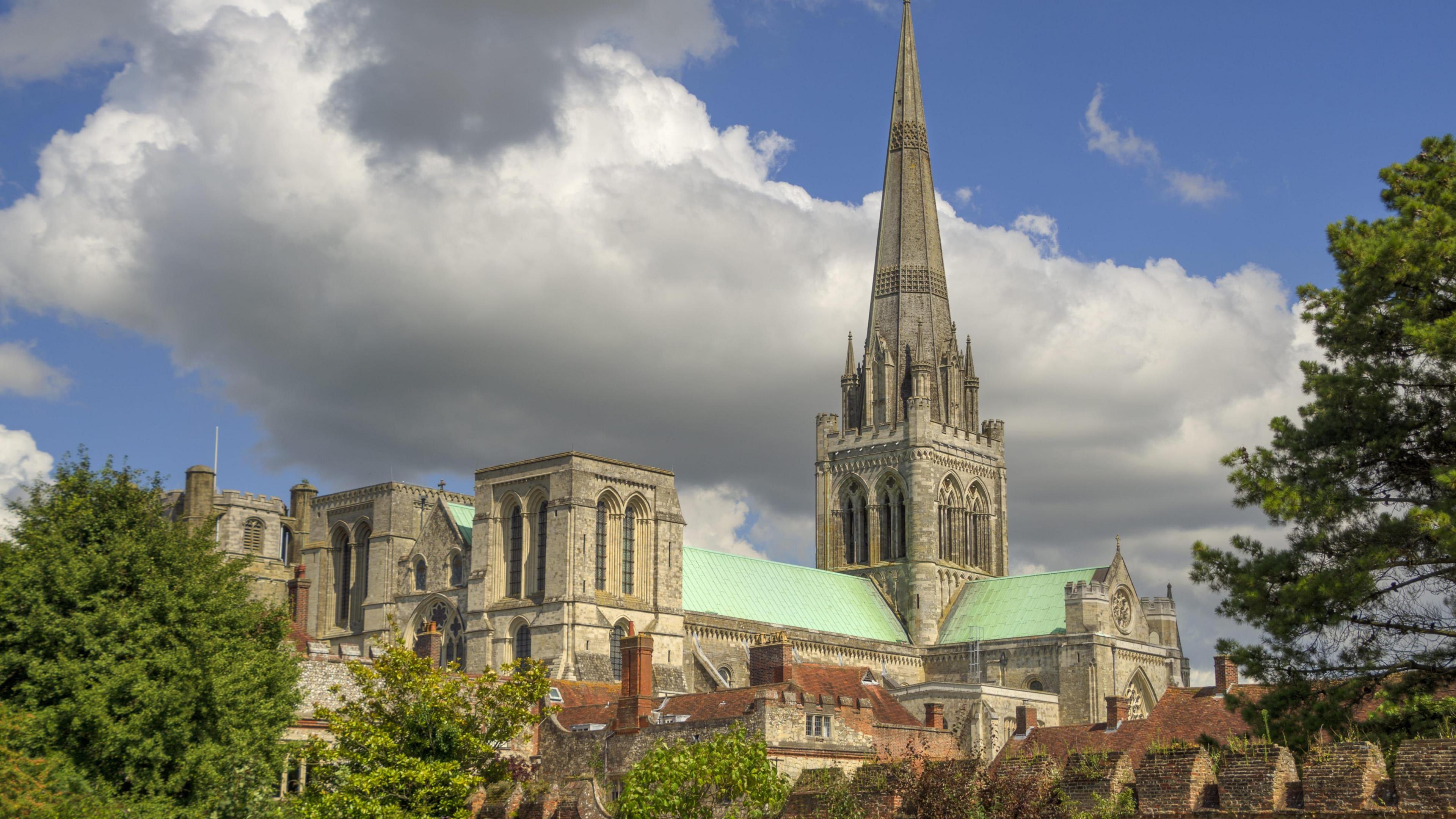 Exterior shot of Chichester Cathedral with trees either side and blue skies and cloud