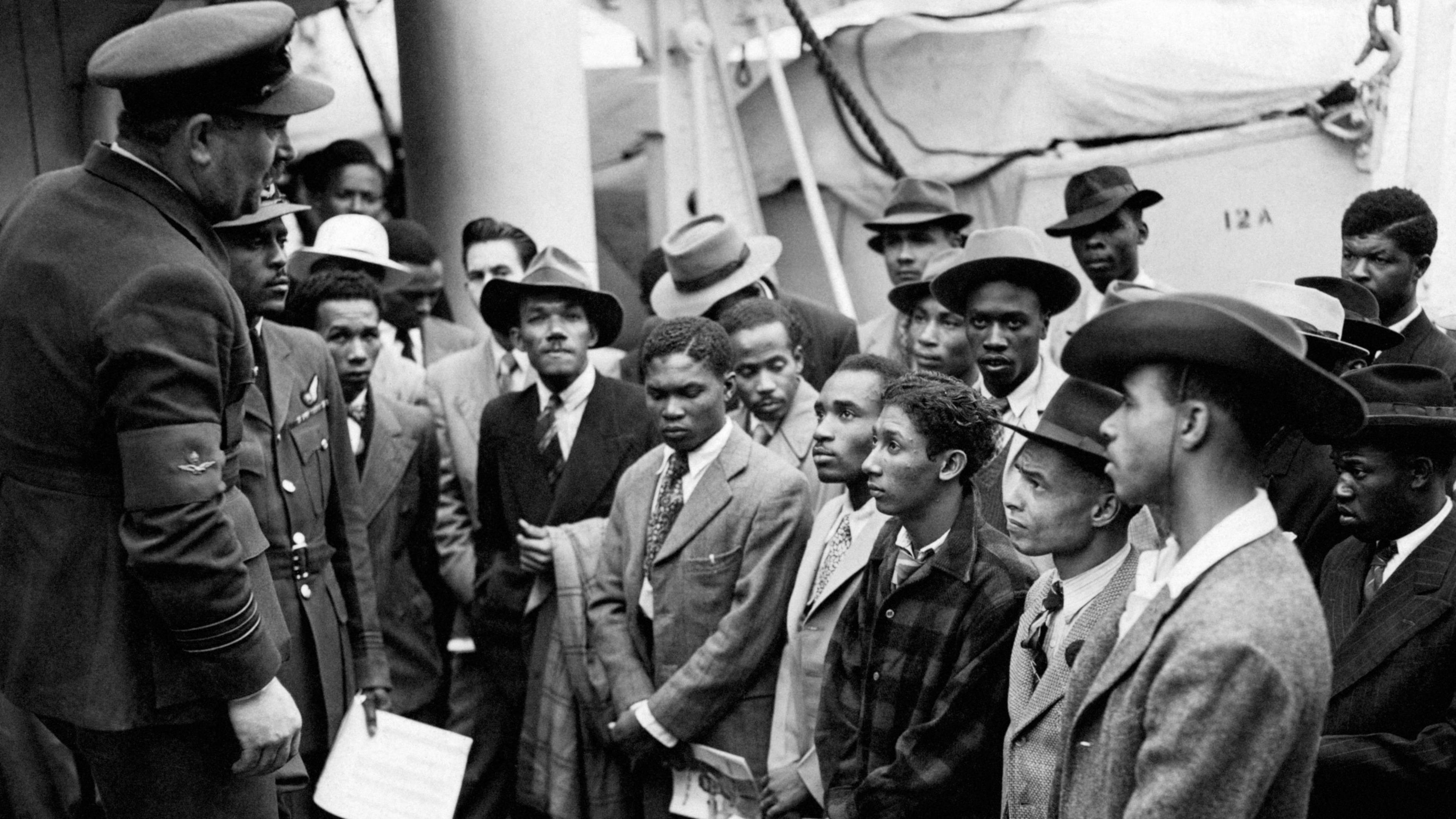 Black and white image of a row Jamaican immigrants welcomed by a RAF official from the Colonial Office after the ex-troopship HMT Empire Windrush landed them at Tilbury.