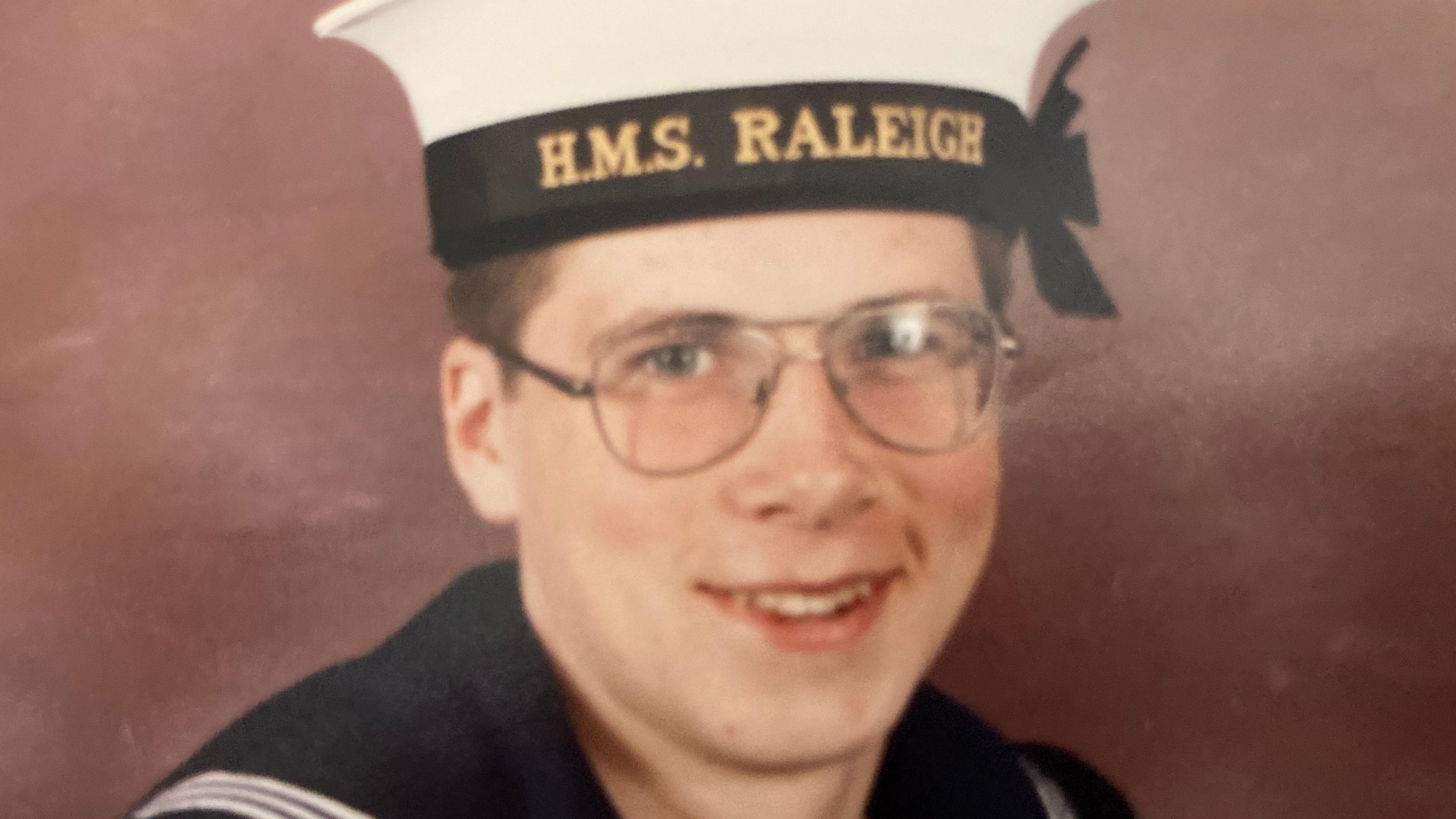 Alex Rasmussen wearing metal glasses and an HMS Raleigh cap as a new recruit 