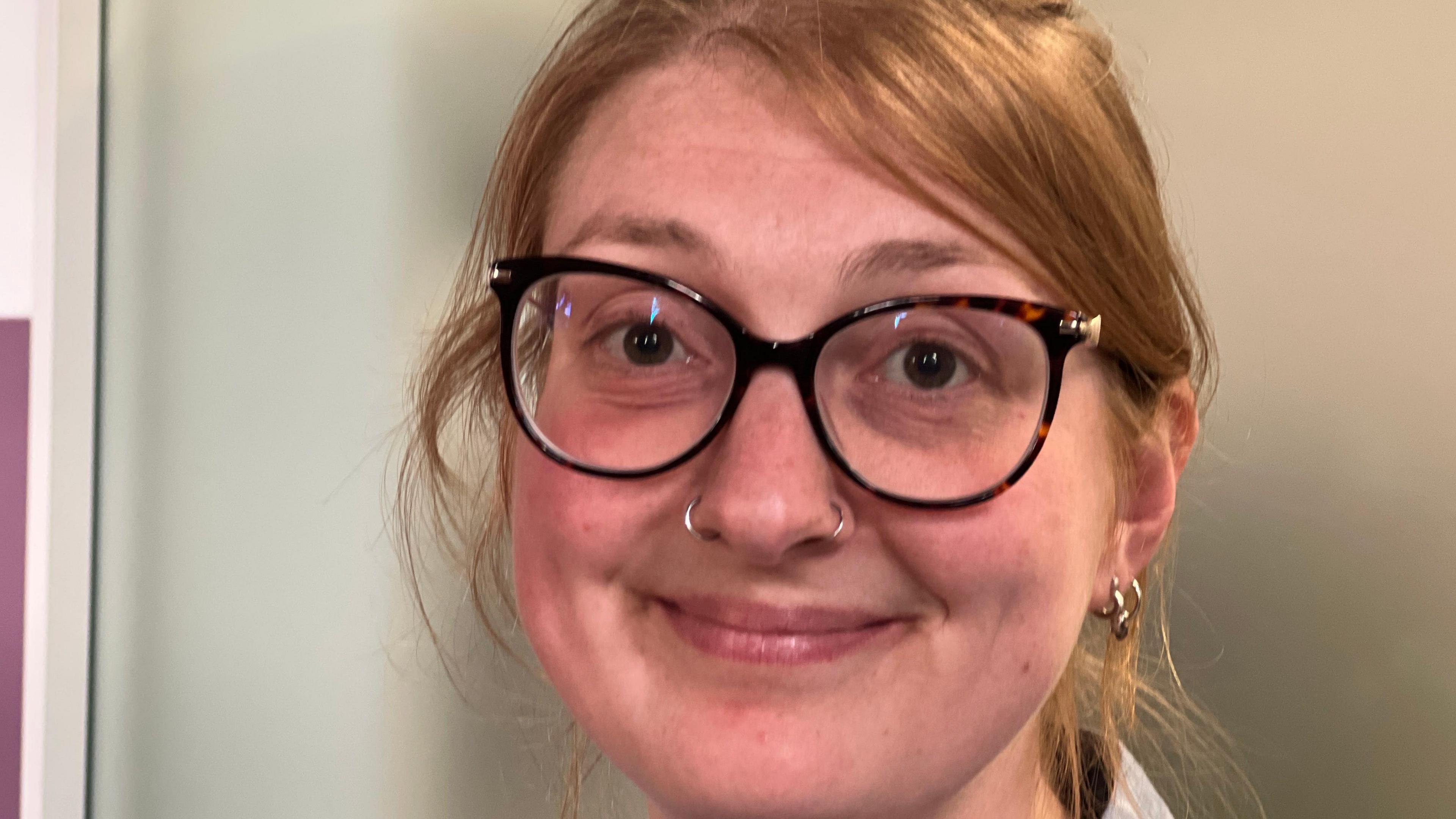 A close up if Serafina's face. She has tied back ginger hair and is wearing dark rimmed glasses and is smiling at the camera.