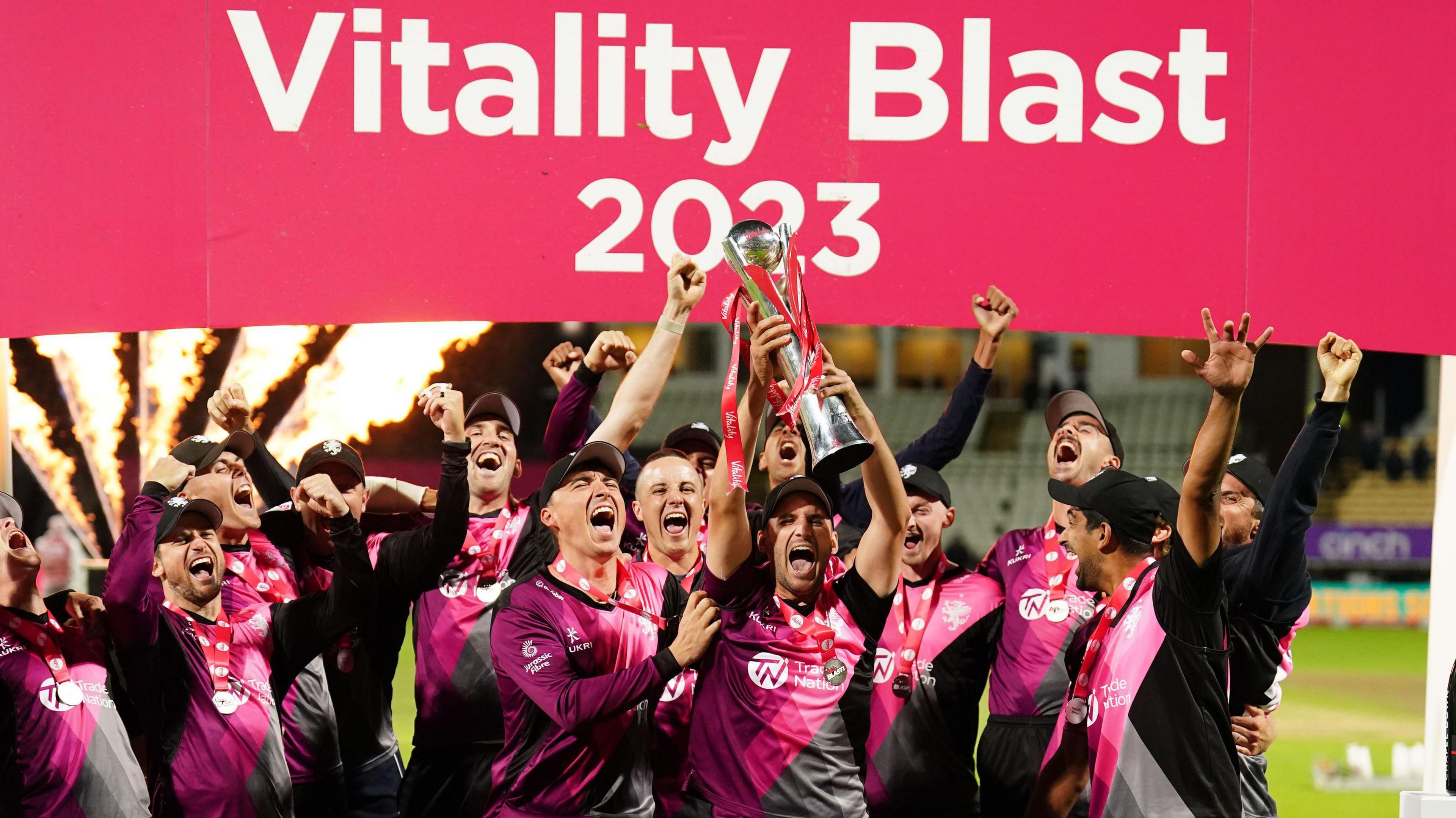 Somerset players celebrate on the podium as the trophy is held in the air and fireworks go off behind them, after winning the 2023 T20 Blast 