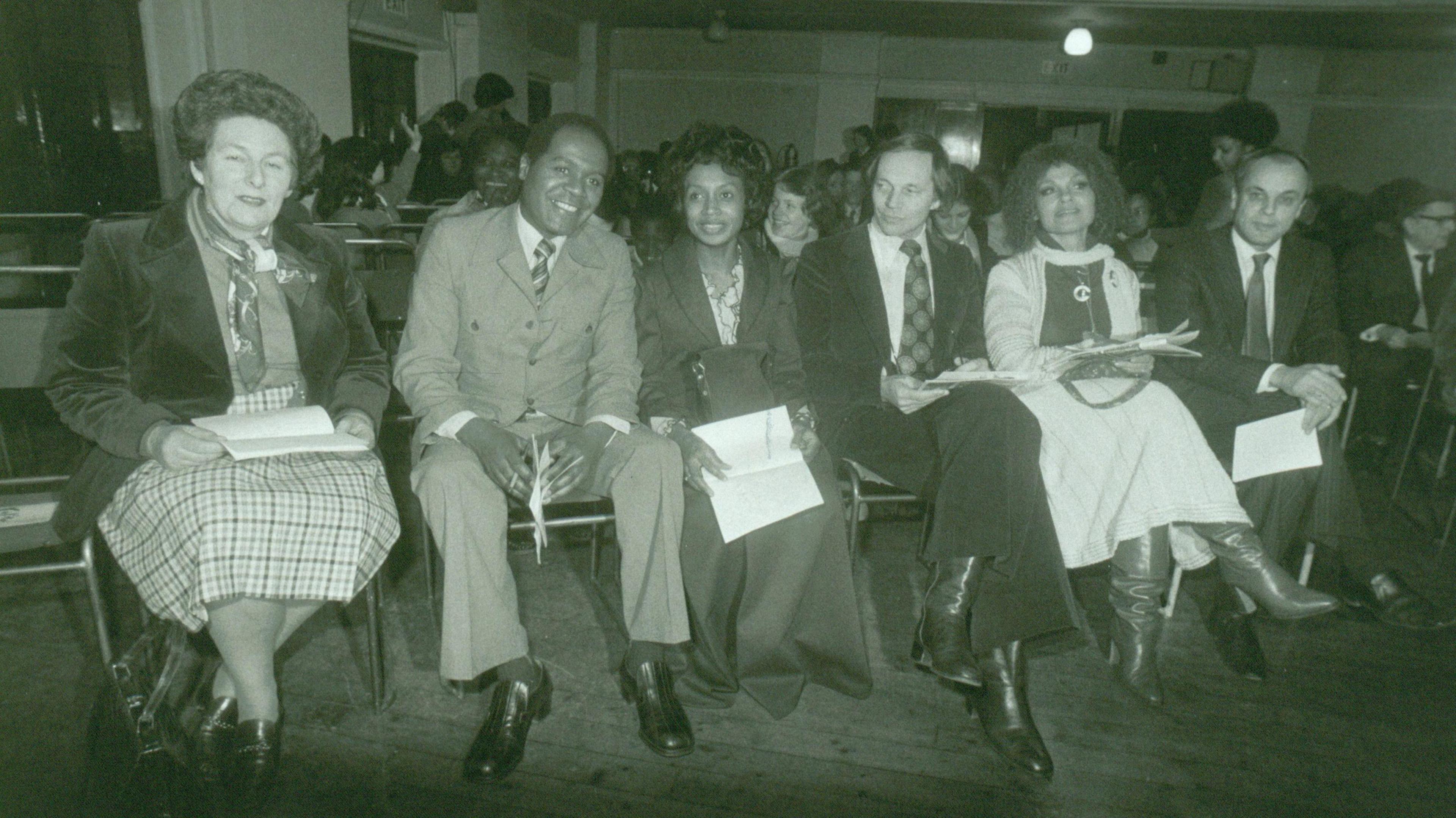 Dr and Mrs Stephenson (second and third left) sit with Paul Dankworth and Cleo Laine (to their right). They are sat in what appears to be a large hall, as though they are about to watch a performance, and are all dressed smartly. 