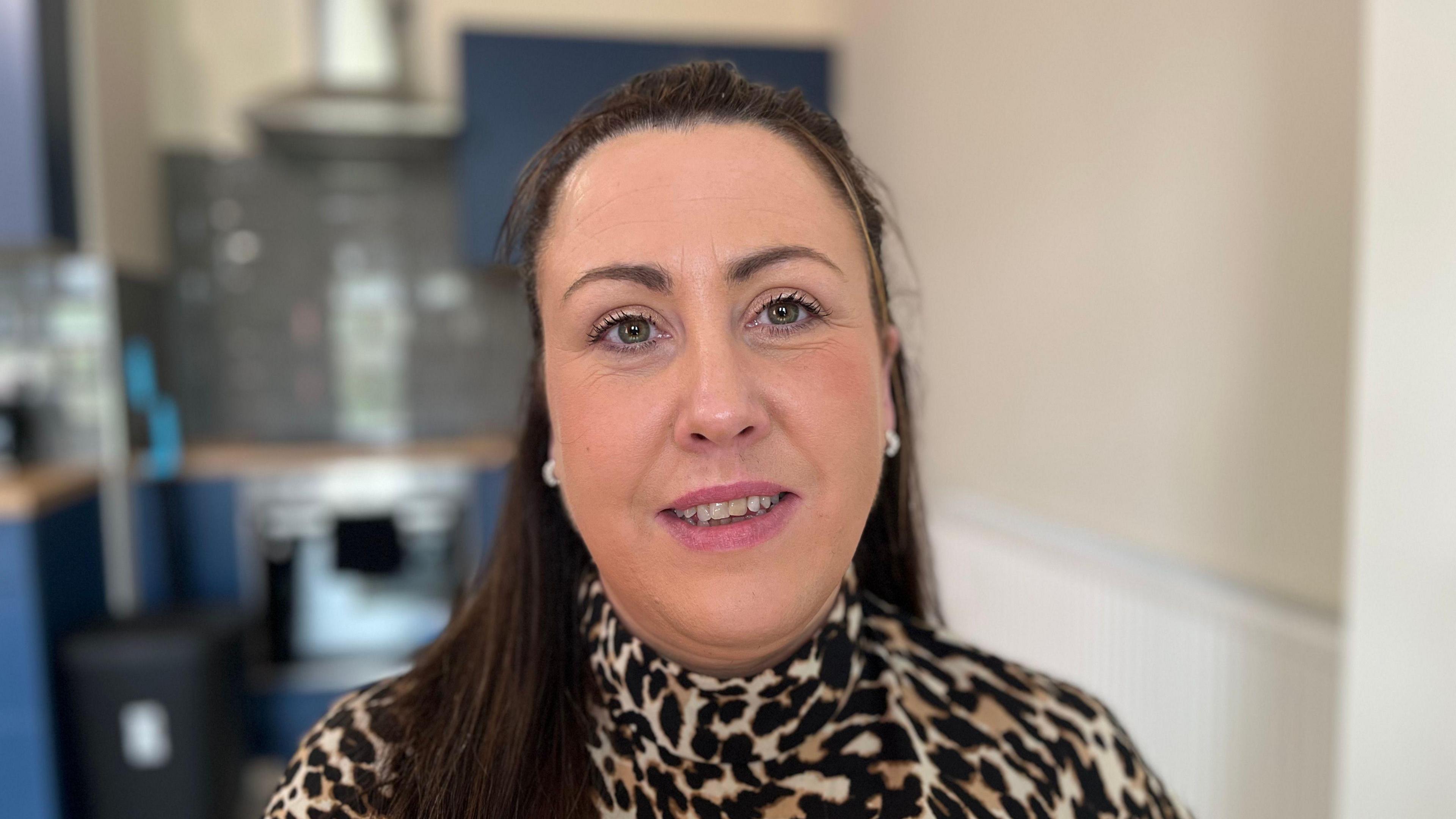 Fiona Boyd sits in the office and looks at the camera with a slight smile on her face. She has long brown hair and a leopard print top