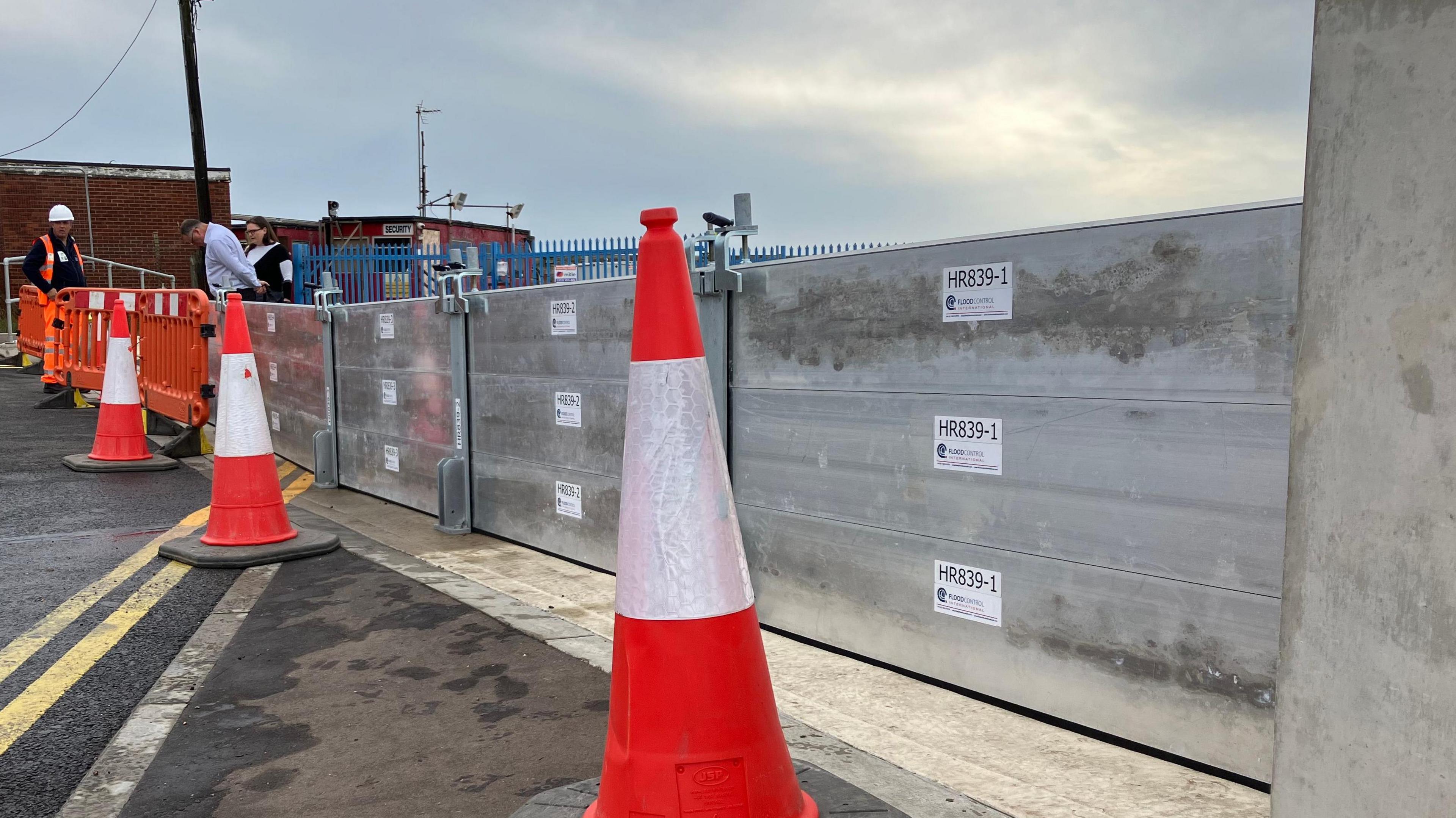 Three cones positioned in front of a large metal barrier spanning from the left to the right of the image.