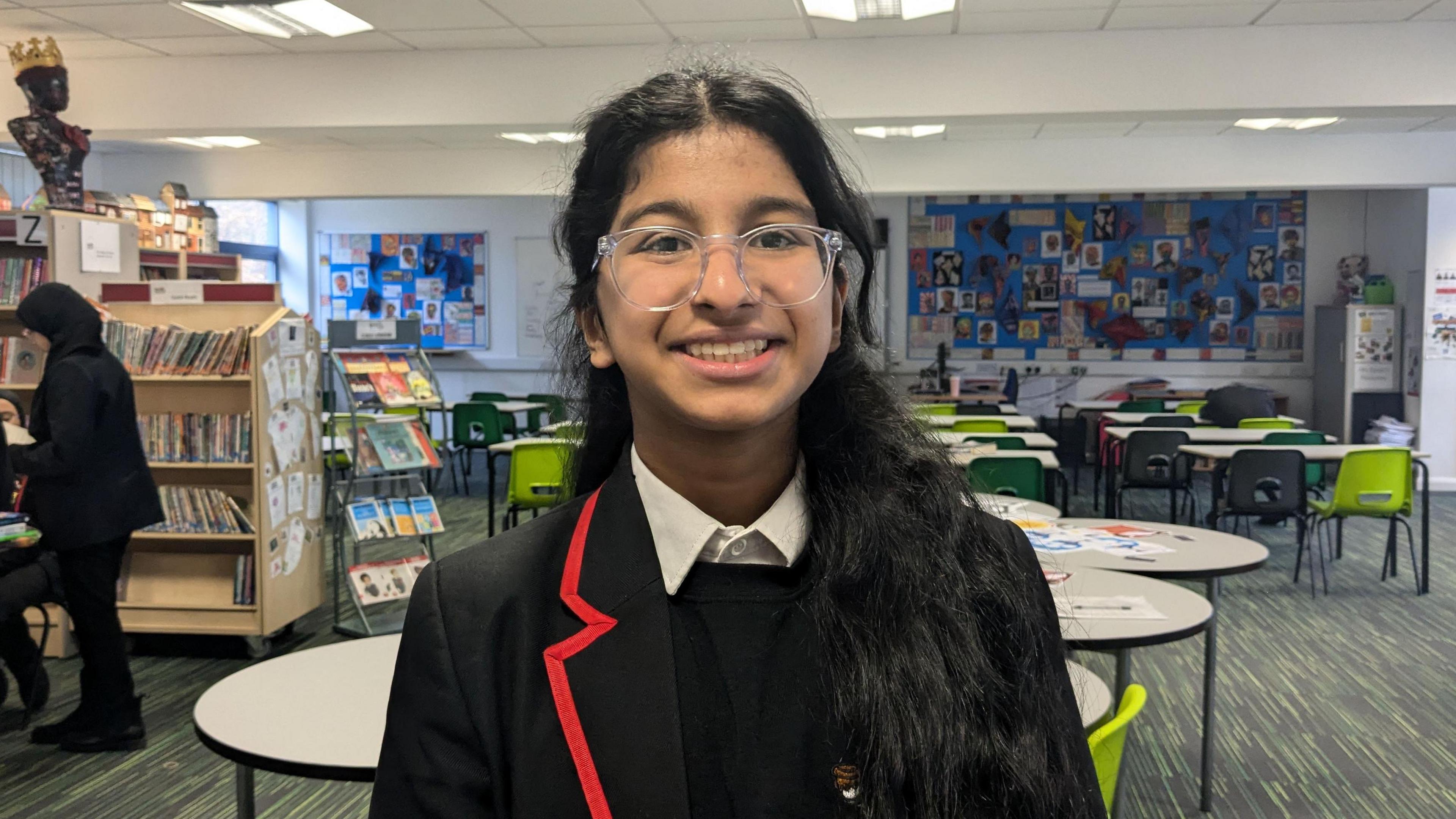 A girl with black hair and clear glasses wearing school uniform and smiling. 