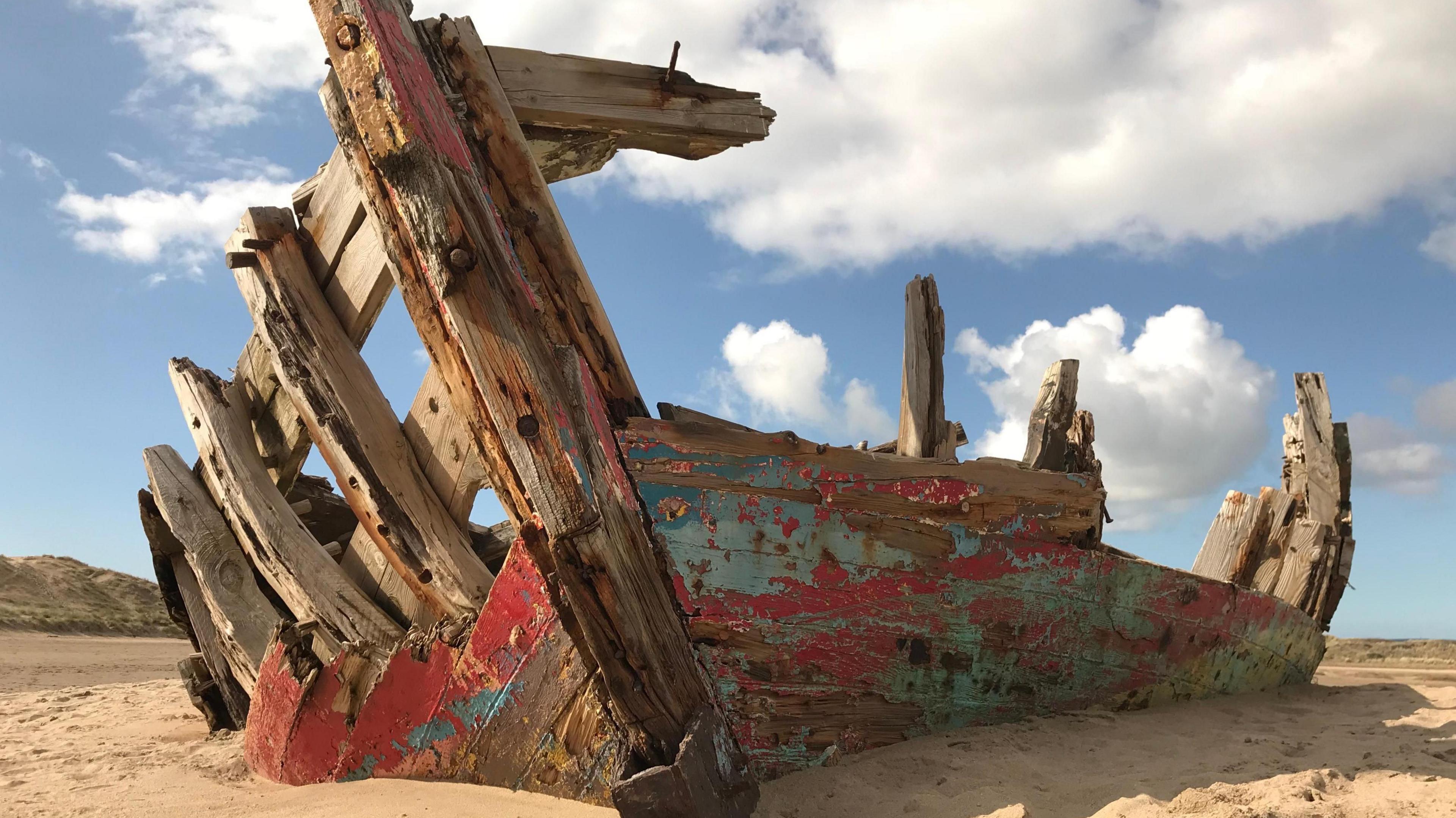 A wooden shipwreck on a beach in Devon. There are clouds in the sky.