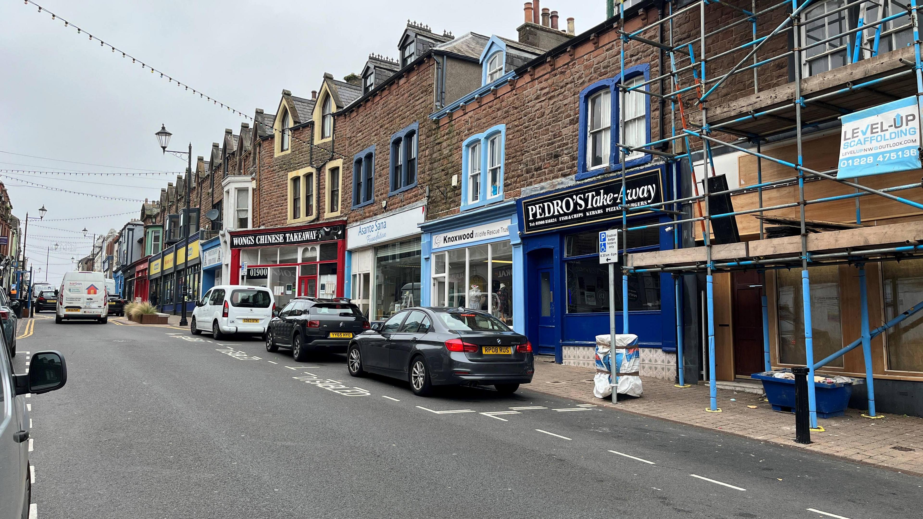 A general view of Senhouse Street in Maryport, with shops lining the street and cars parked outside.