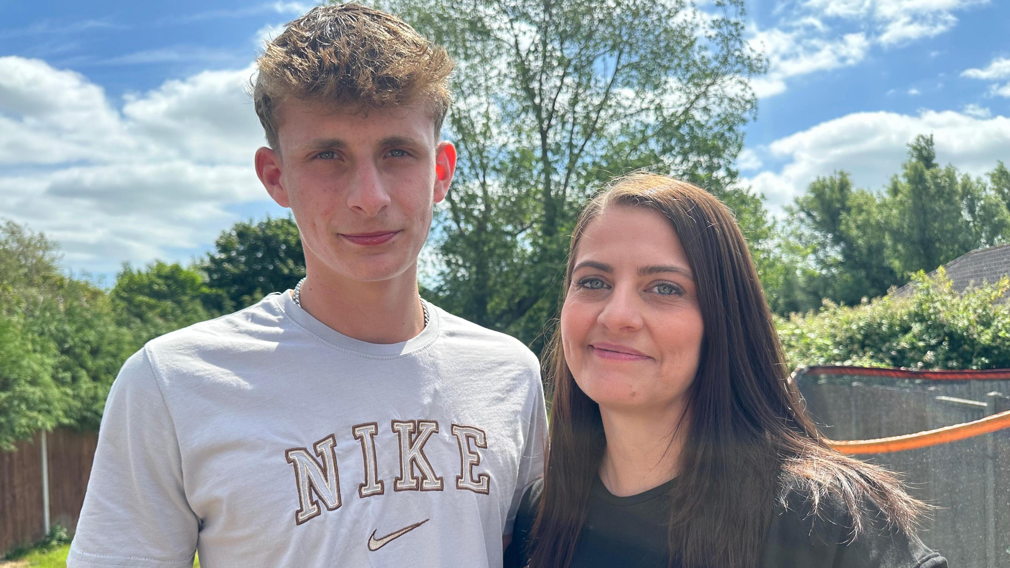 A close-up image of Luca and his mum in the garden, slightly smiling. The pair have blue eyes. Luca has blond hair and Jemma has brown hair. Jemma is on the right of Luca.
