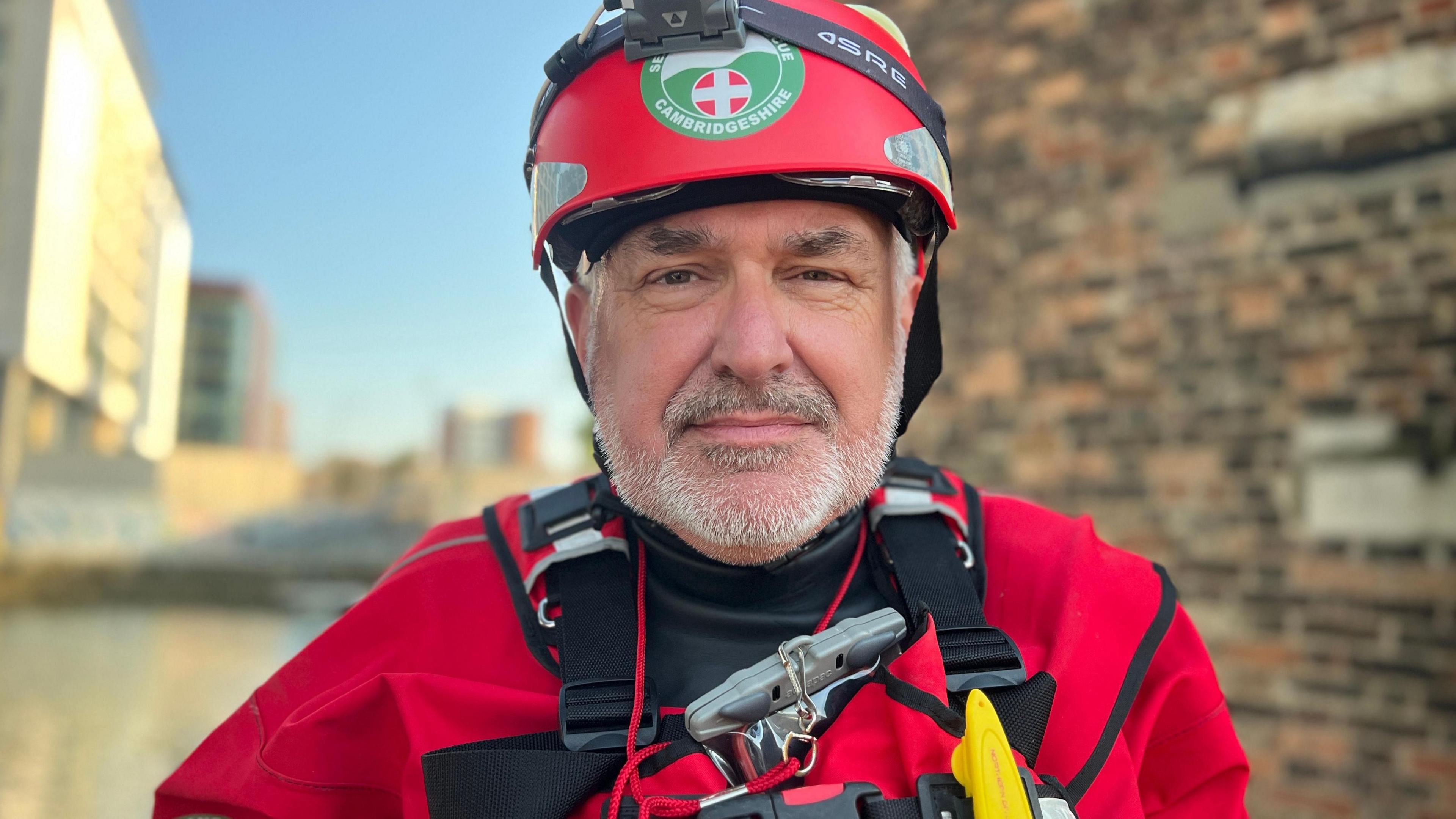 Barry Carter wearing red uniform of Cambridgeshire Search and Rescue looking at camera