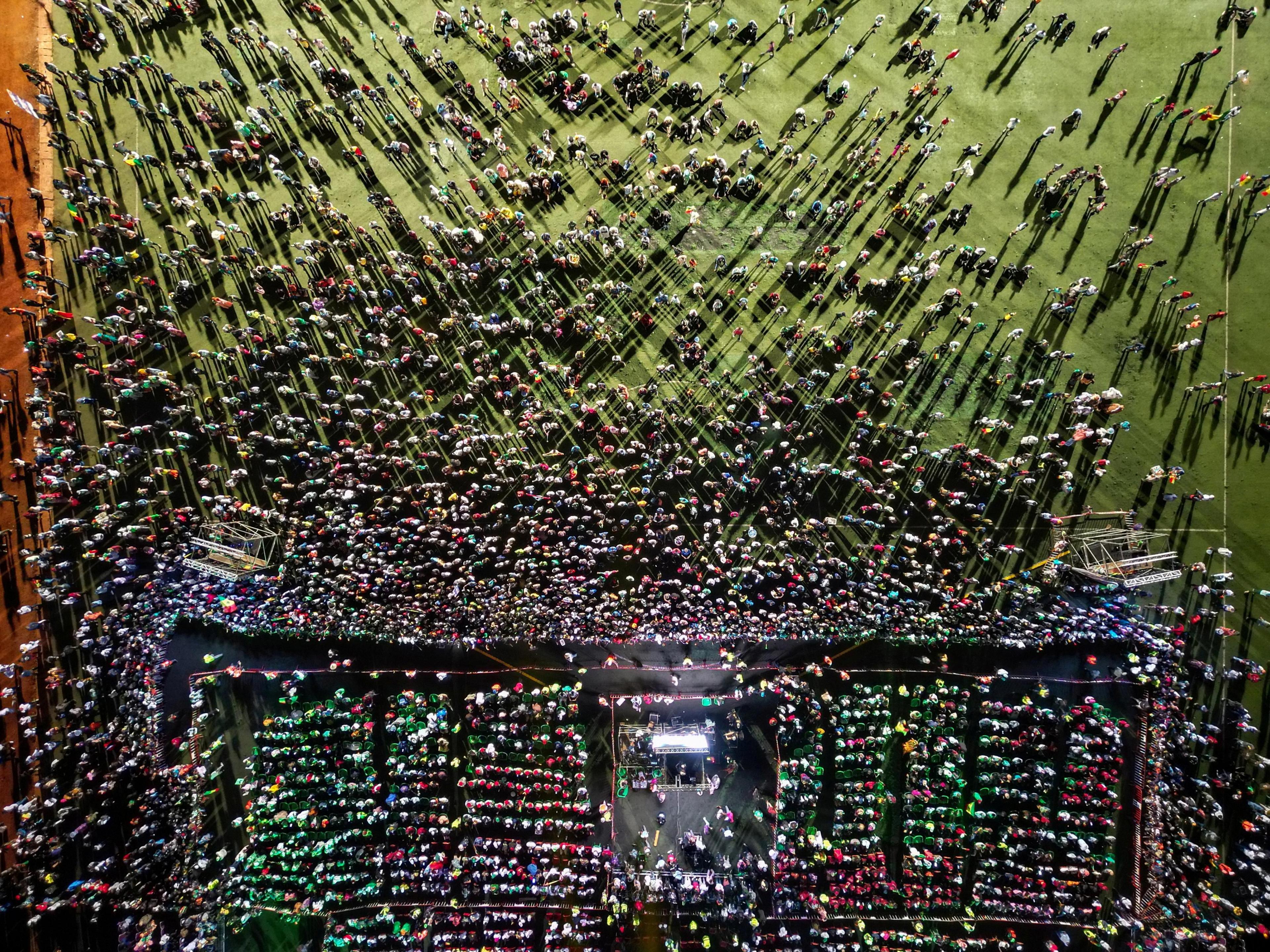 
A drone view shows people near a stage in a large field. 