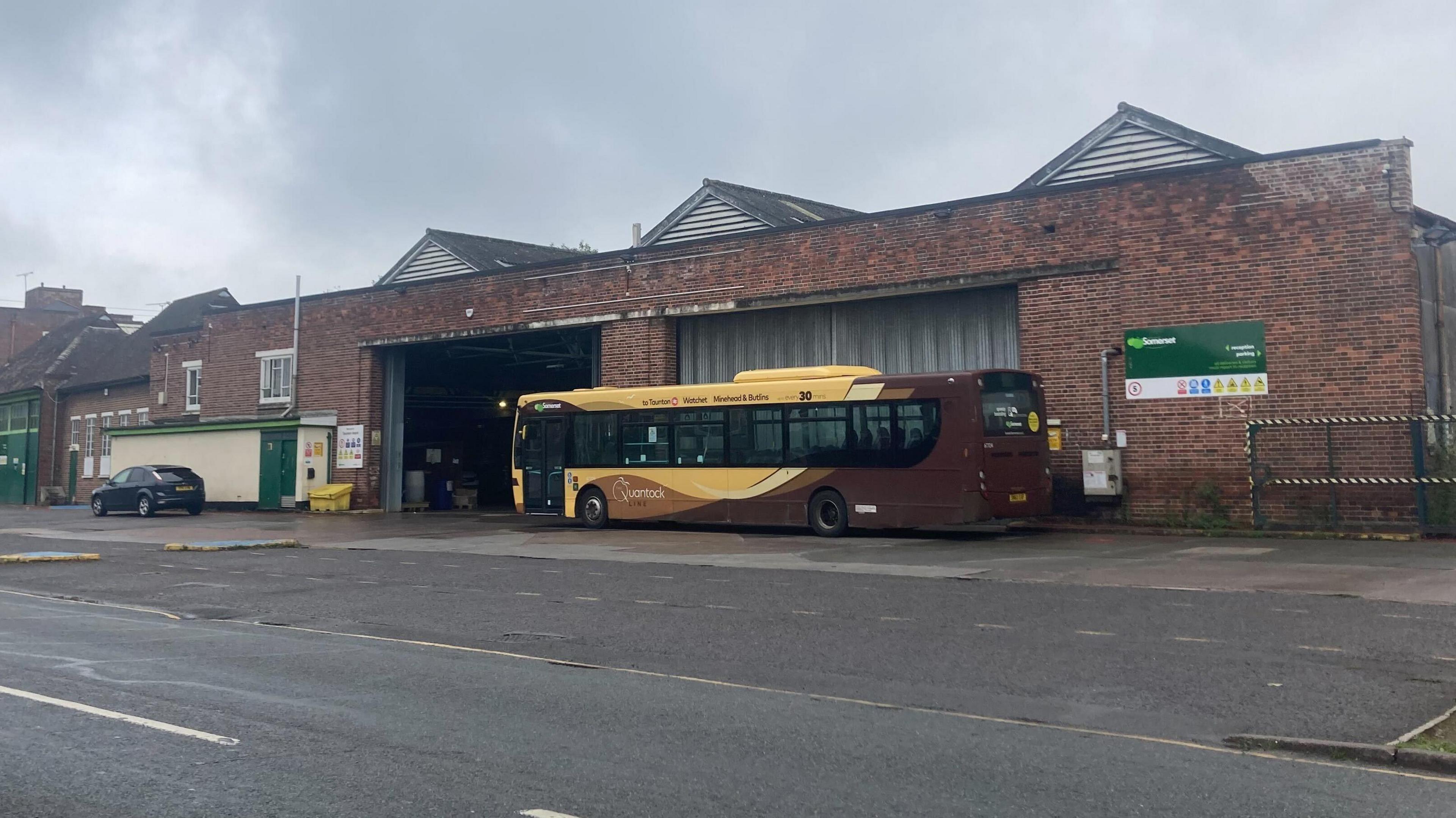 a brown and beige single decker bus parked outside a brick building