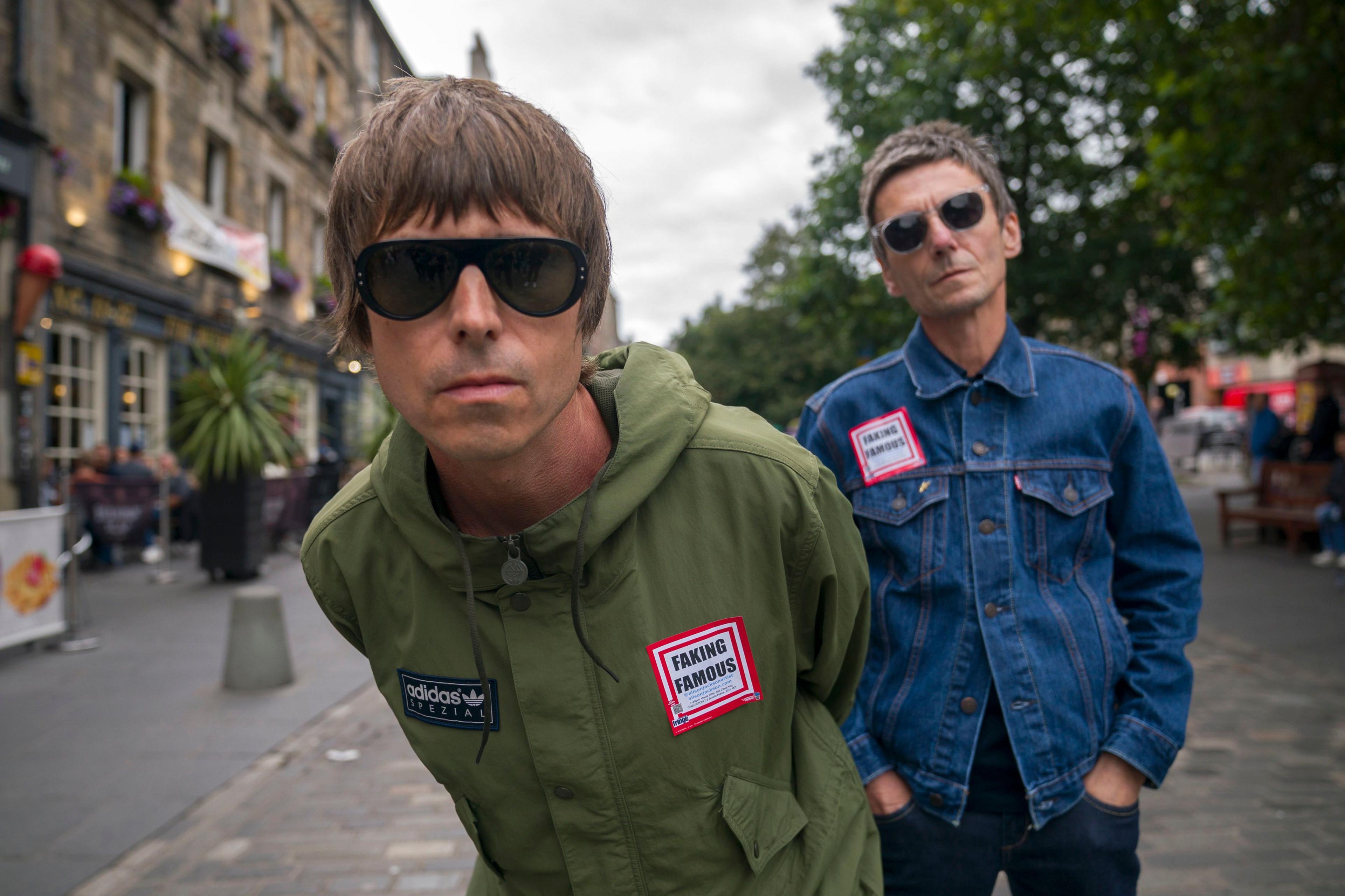 Lookalikes of Liam and Noel Gallagher get into character in The Grassmarket, Edinburgh. "Liam" is in a khaki Adidas jacket and "Noel" in a denim jacket. Both are wearing shades.