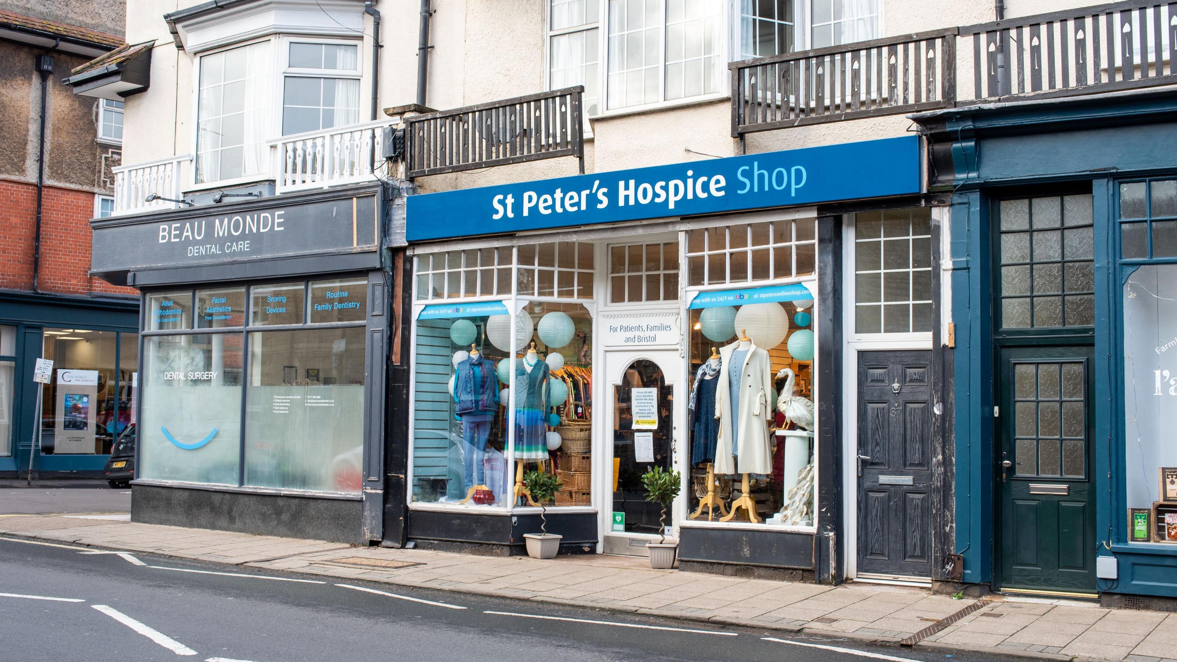 The St Peter’s Hospice shop in Westbury Park, as seen from across the street. The store signage is blue, and the decorations and mannequins in the window also follow a blue theme. There are also light-blue paper lanterns hanging from the ceiling.