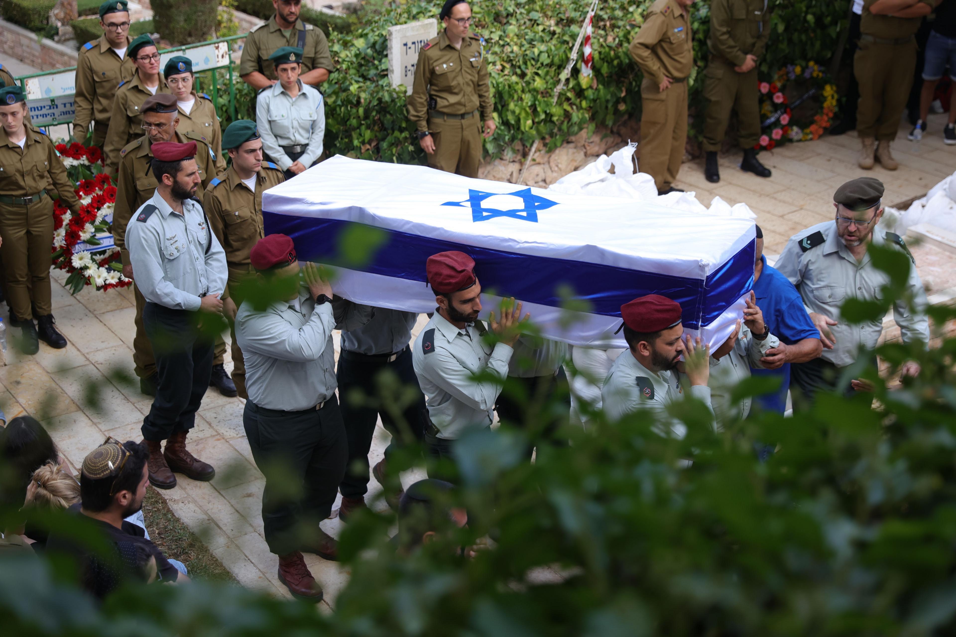 Israeli soldiers carry the coffin of Israeli soldier Tal Cohen during his funeral at Mount Hertzel military cemetery in Jerusalem. The Israeli flag covers the coffin. The photo is taken slightly from above, looking down on the occasion.
