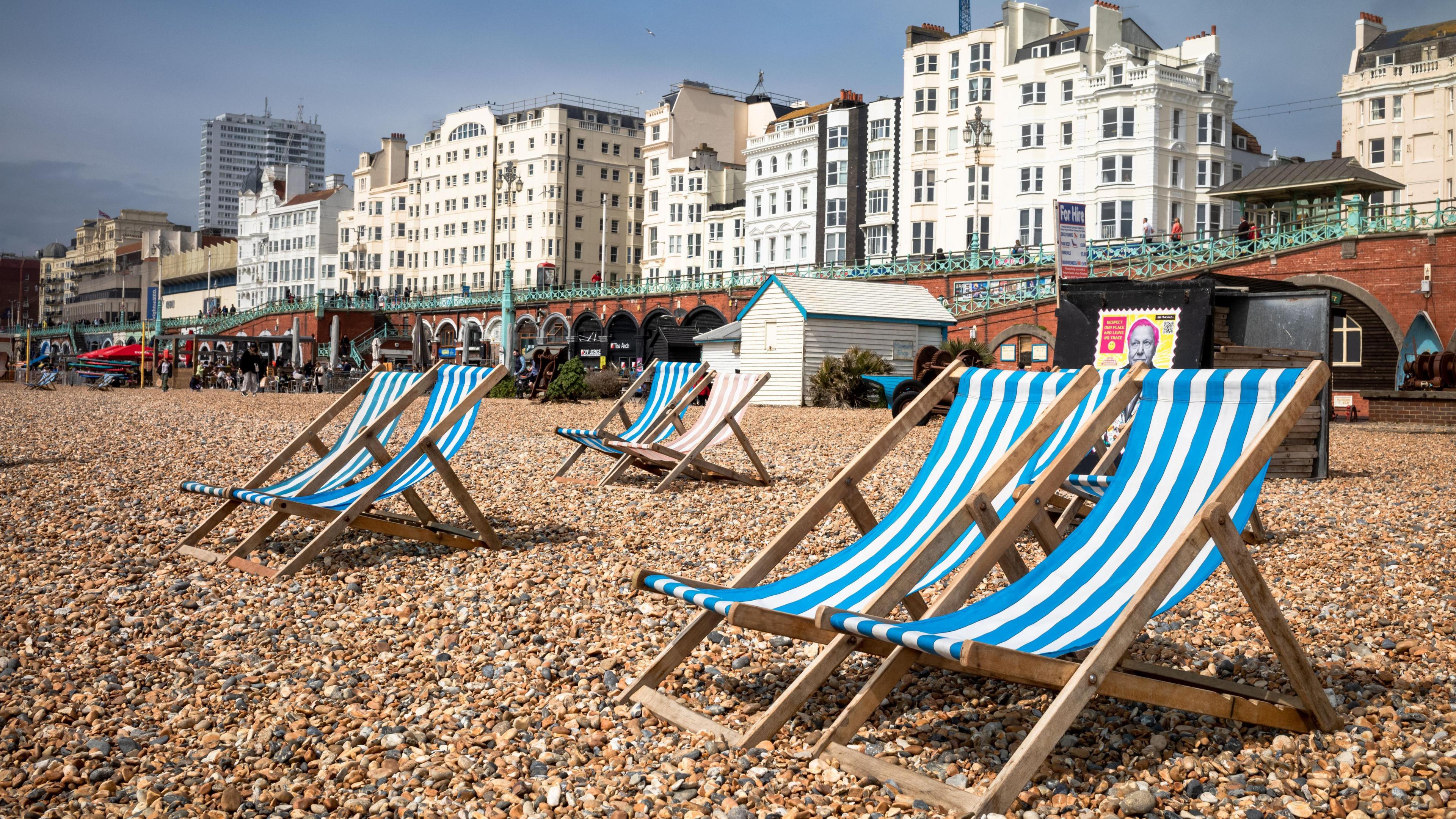 Blue and white striped deck chairs sit on the pebbles on the seafront in Brighton city centre.