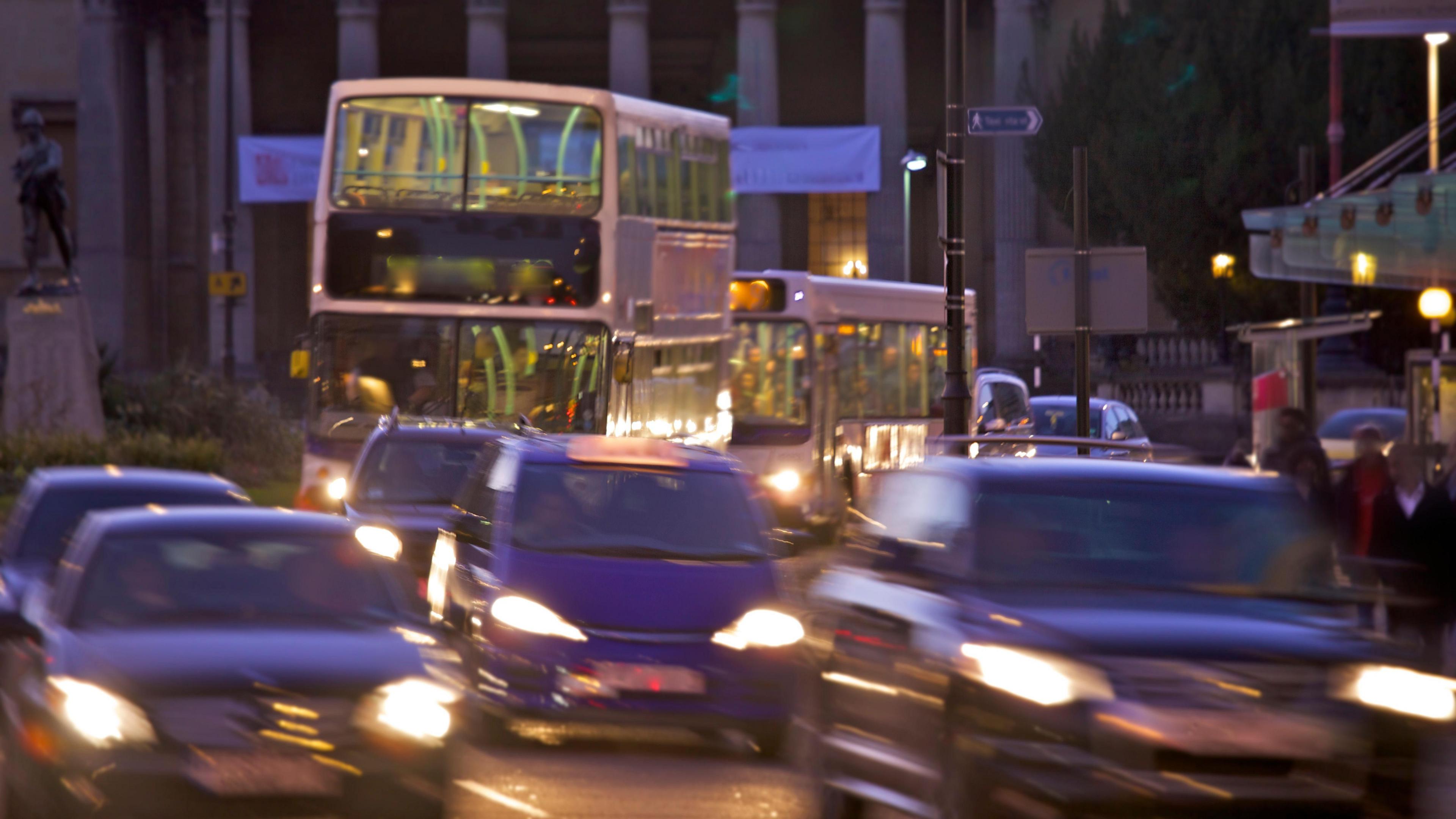 Traffic in Bristol city centre. The cars are blurry as they're moving. Two buses can also be seen.