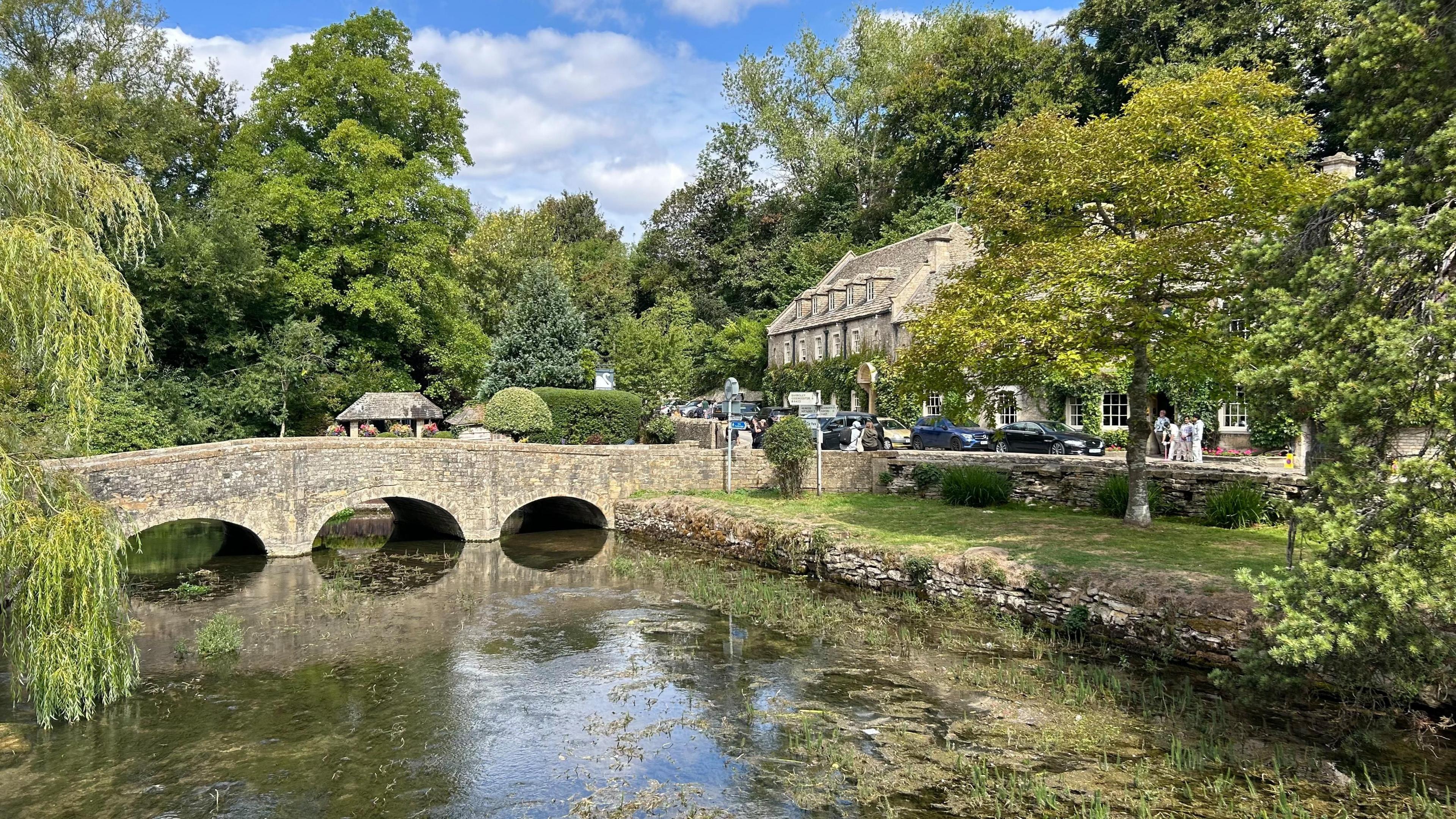 A scene looking over a river. A brick bridge with arches is in the distance. There is a large, old building to the right