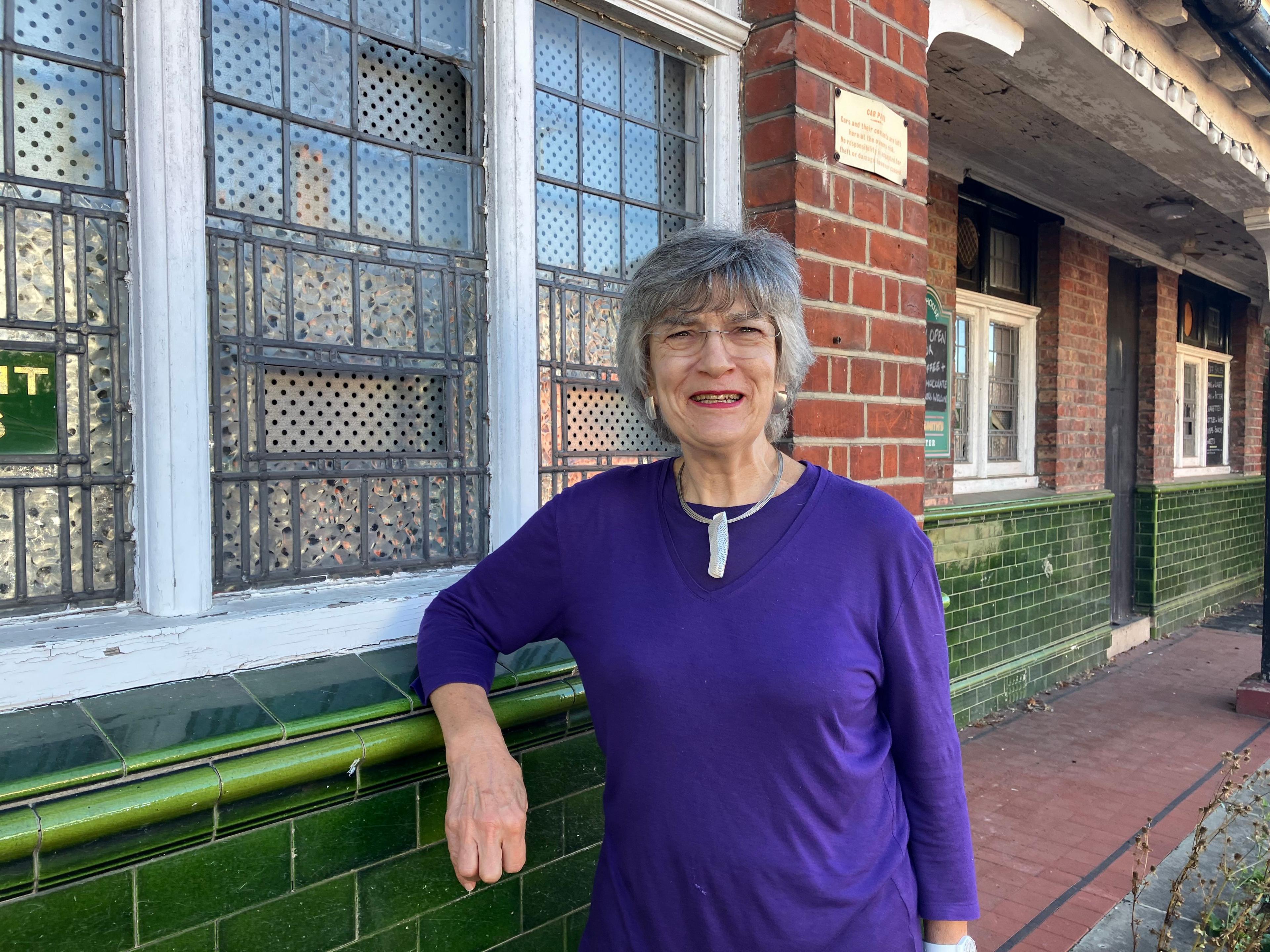 Leo Tye, a woman with short grey hair and wearing a purple dress, leans on the window of the former Winning Horse pub.