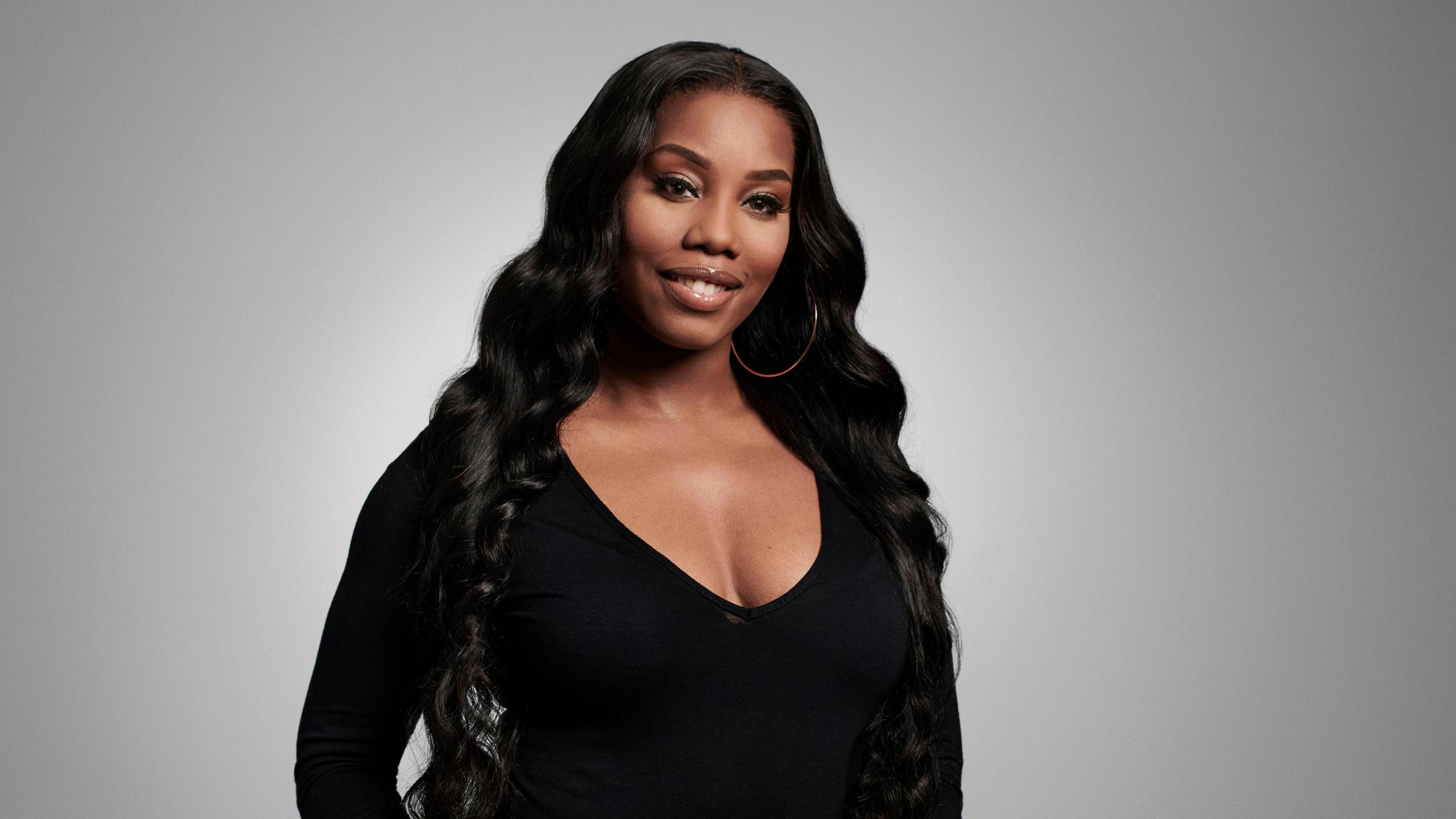 1Xtra presenter Nadia Jae wearing a black top, smiling, with a grey background