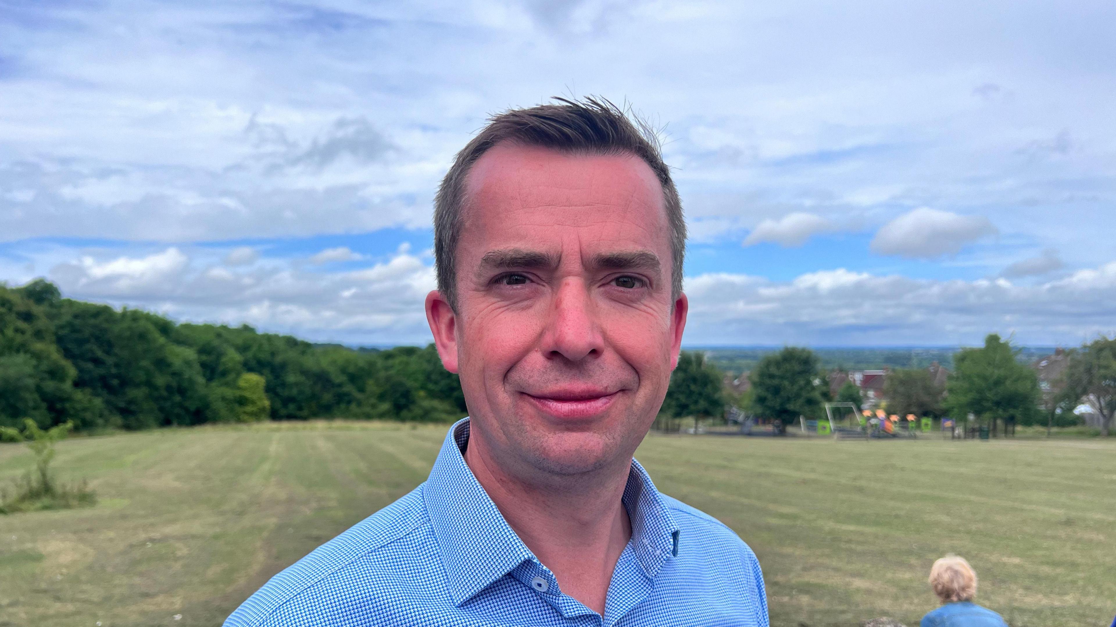 Callum Miller from the shoulders up. He is wearing a blue shirt and has a park in the background behind him.