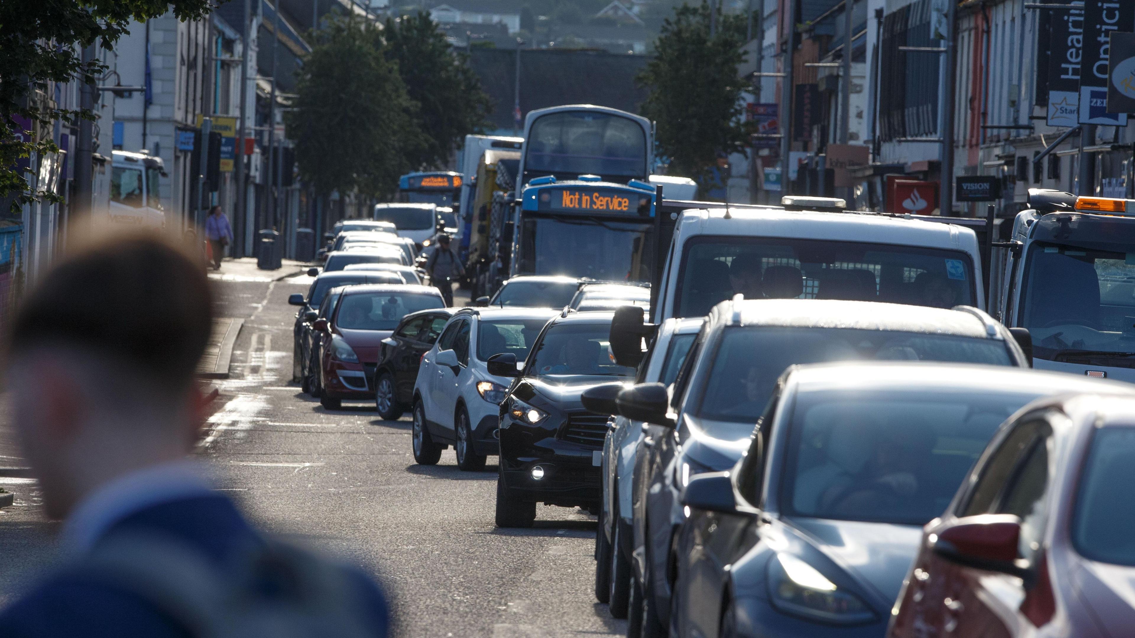 A row of traffic in a street with rows of shops and businesses on either side