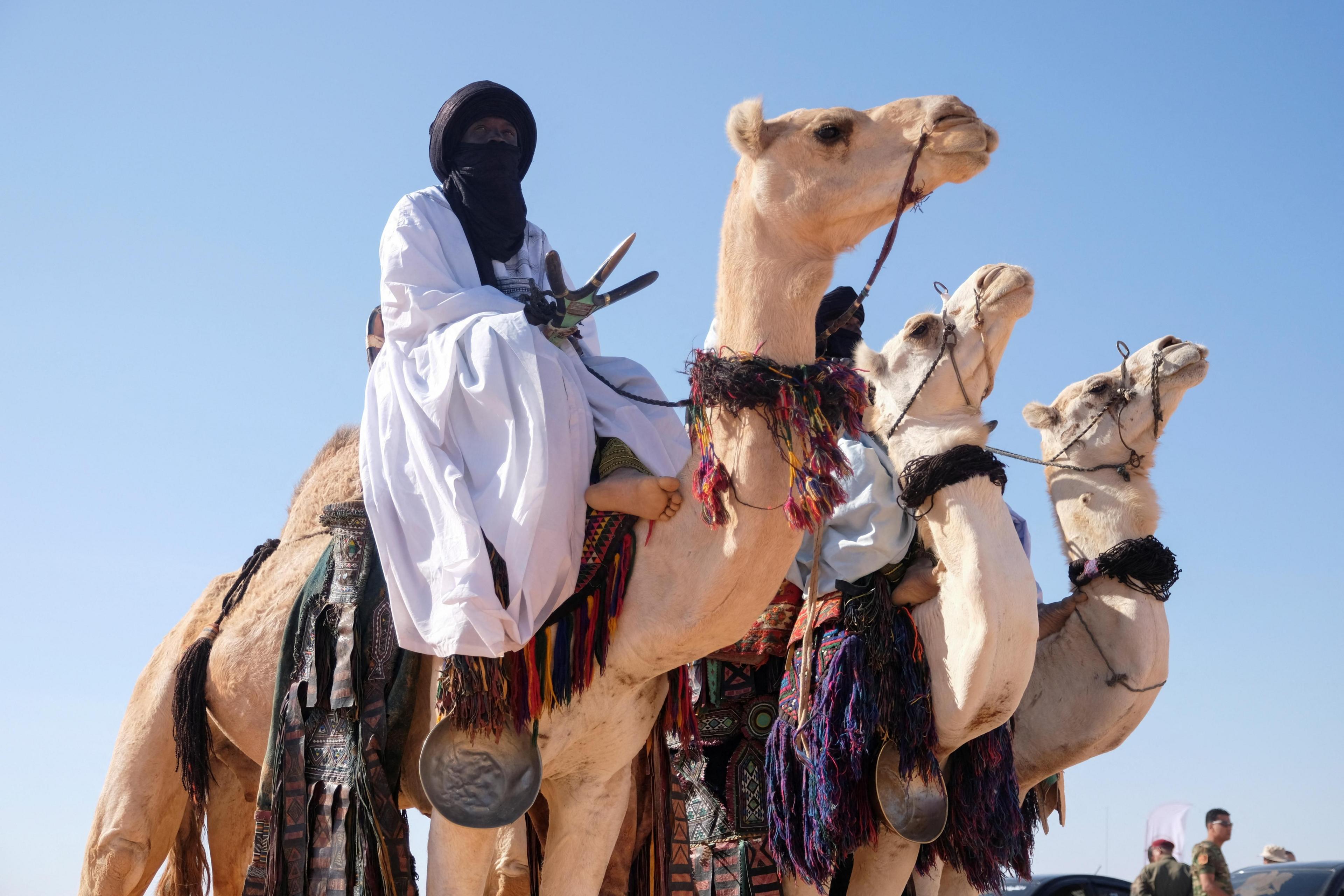 Men wearing traditional garb ride camels.