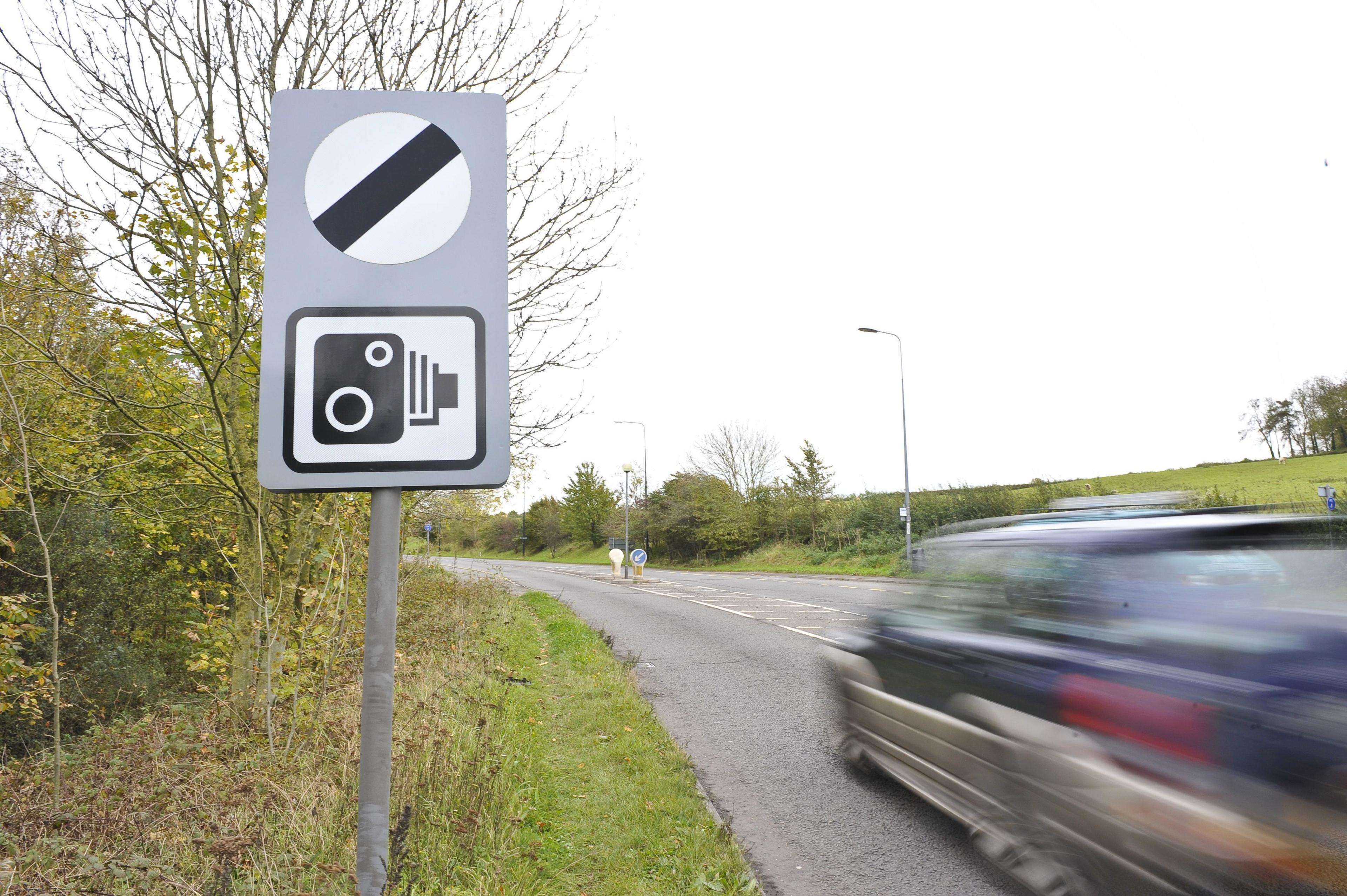 A speed camera sign with a blurry car driving past 