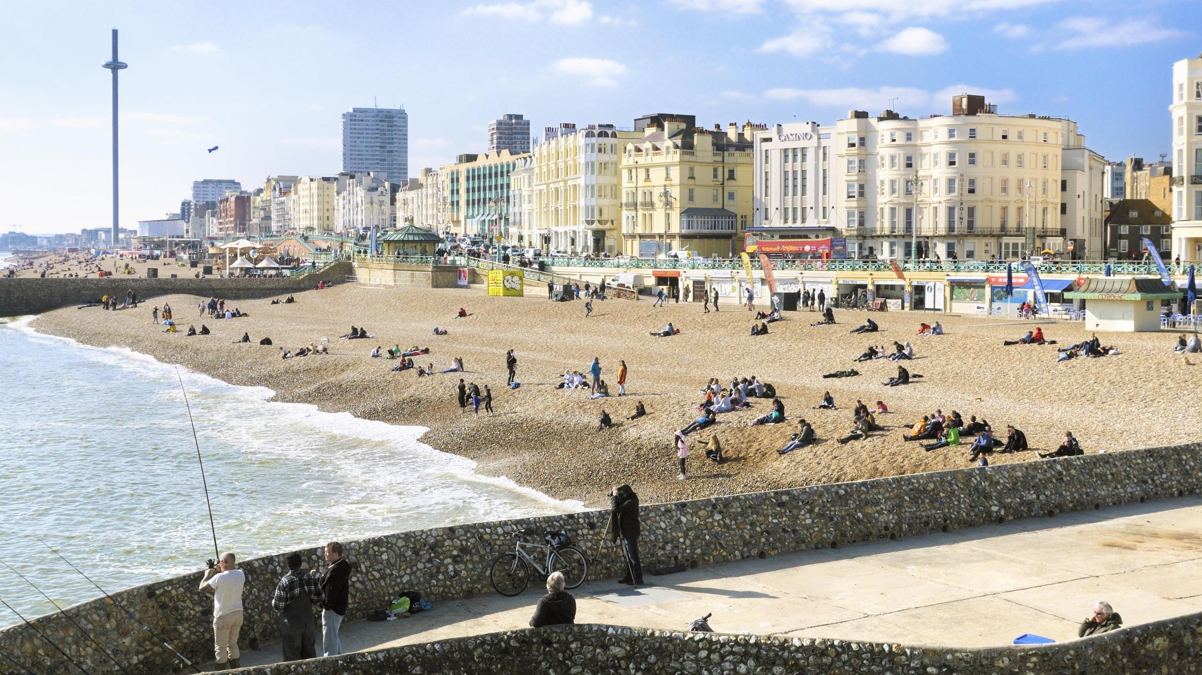 People fishing and laying on Brighton Beach with the promenade and i360 in the background.