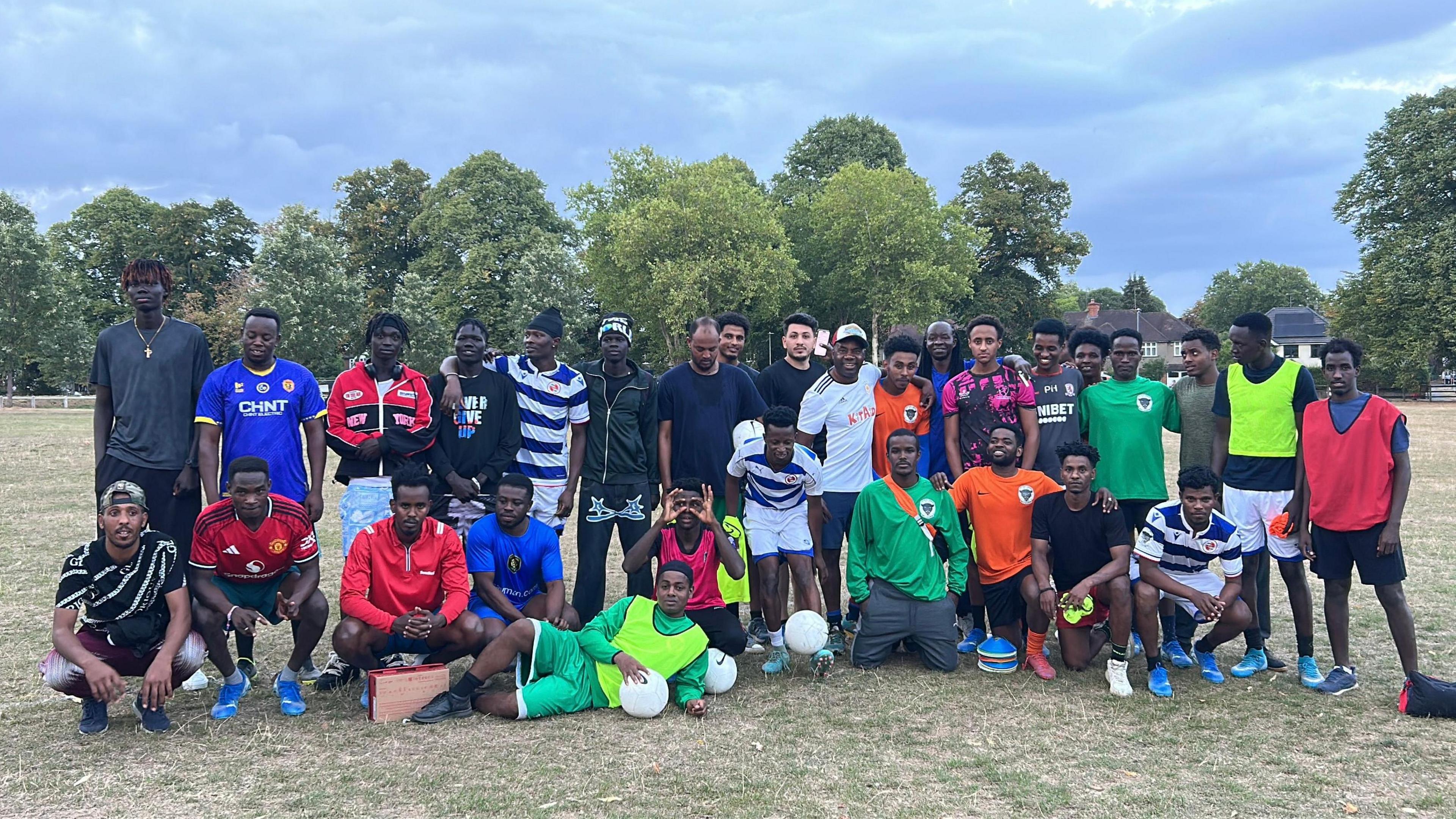 A football team the Sanctuary Strikers, some stood in a line and some knelt or crouched in front of them posing for a team photograph.