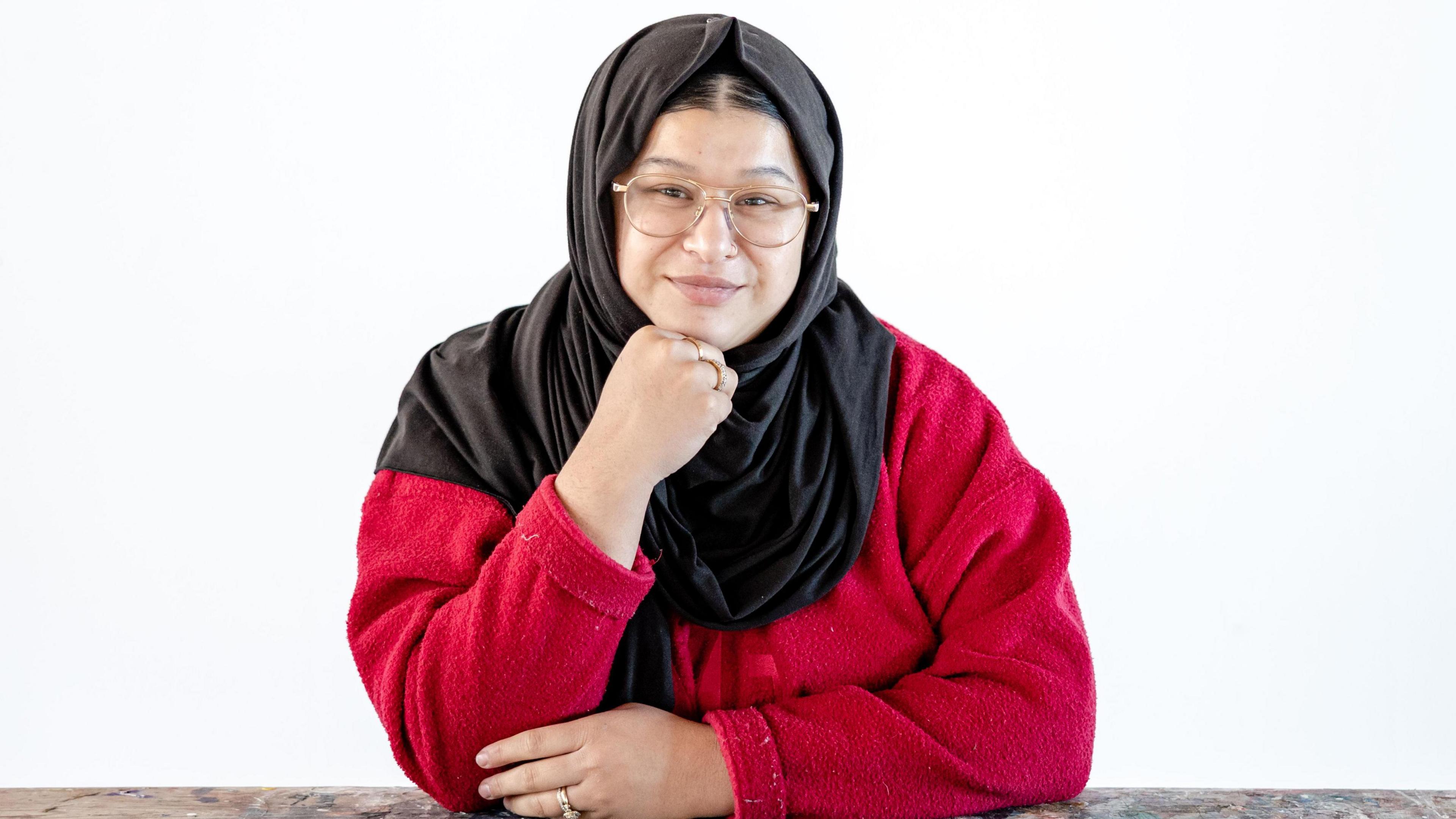 A woman wearing a black headscarf and glasses and a red jumper