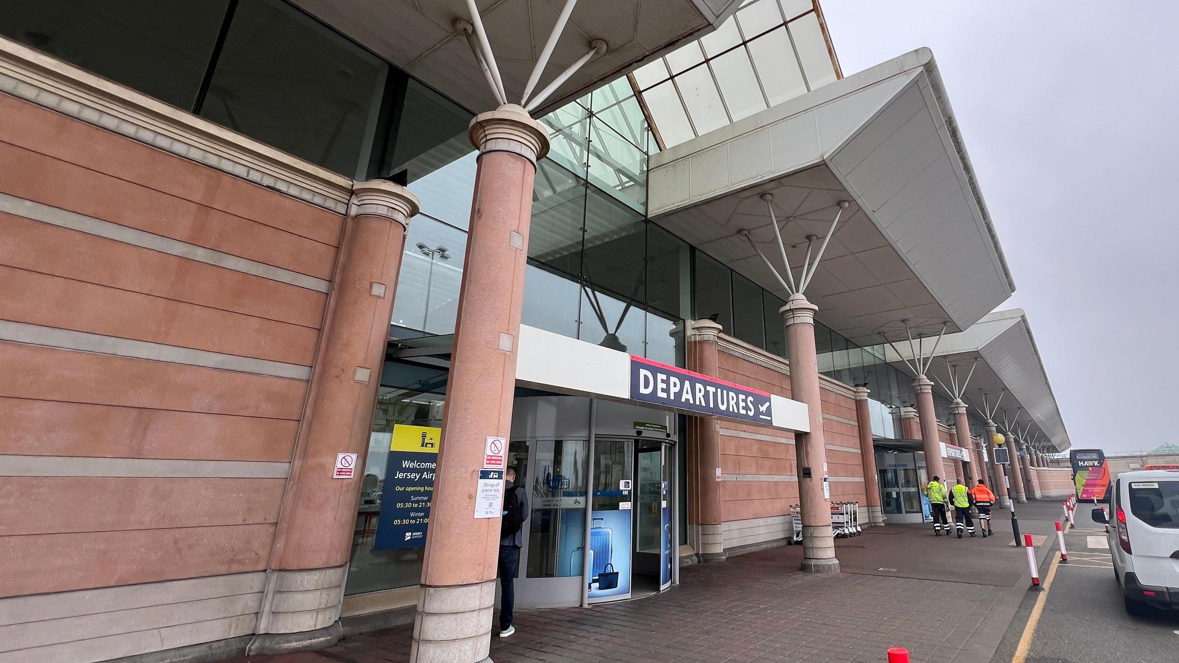 Departures entrance to Jersey Airport. It is a brick building with vehicles parked outside.