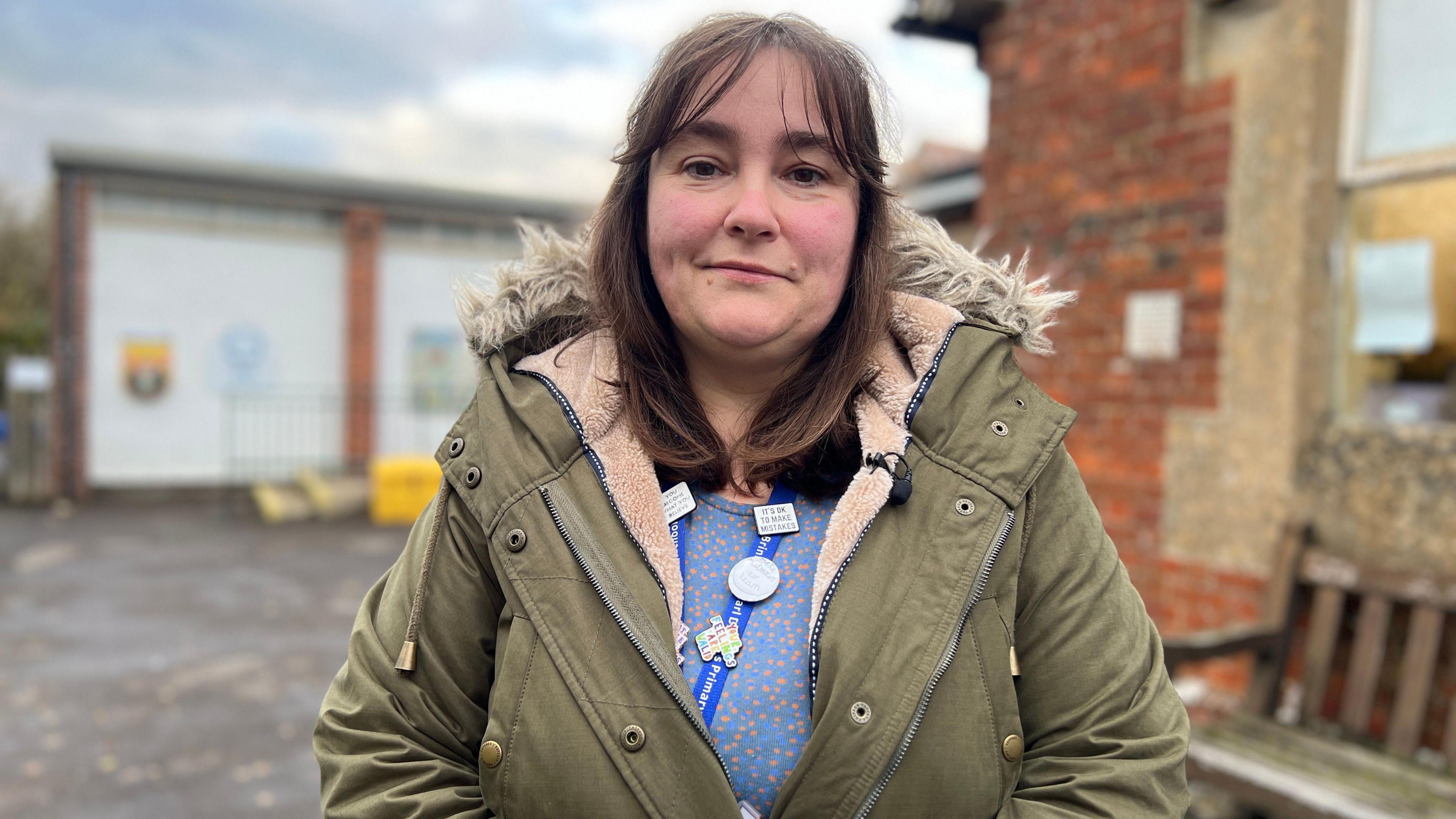 Dauntsey headteacher Alana Walch. She has dark, shoulder length hair and is wearing a blue and pink spotted top with a khaki green parka. She is pictured outdoors, looking directly at the camera and smiling.