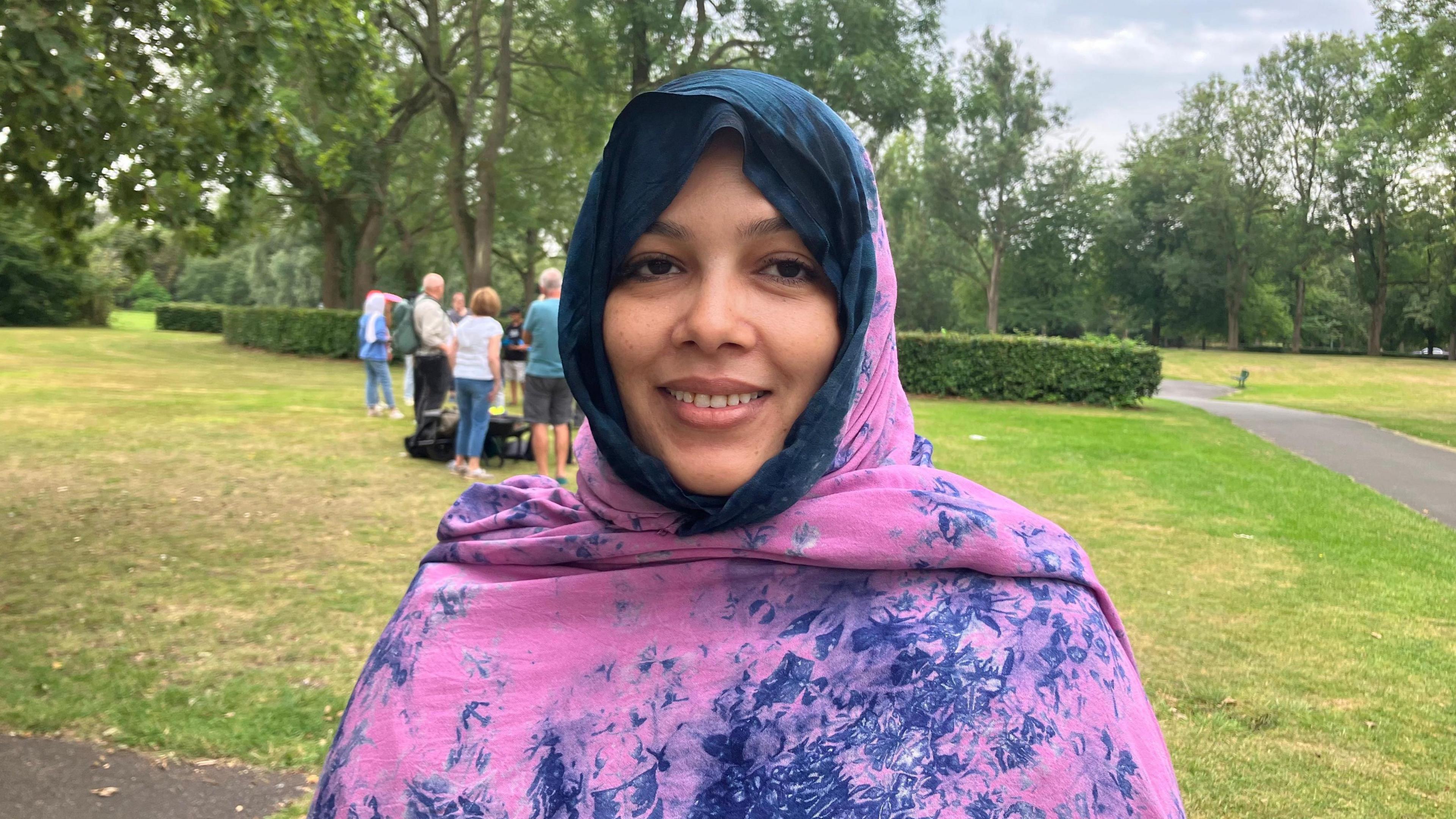 Fatimatu Bachir, wearing a pink and purple shawl, smiles in a Manchester park