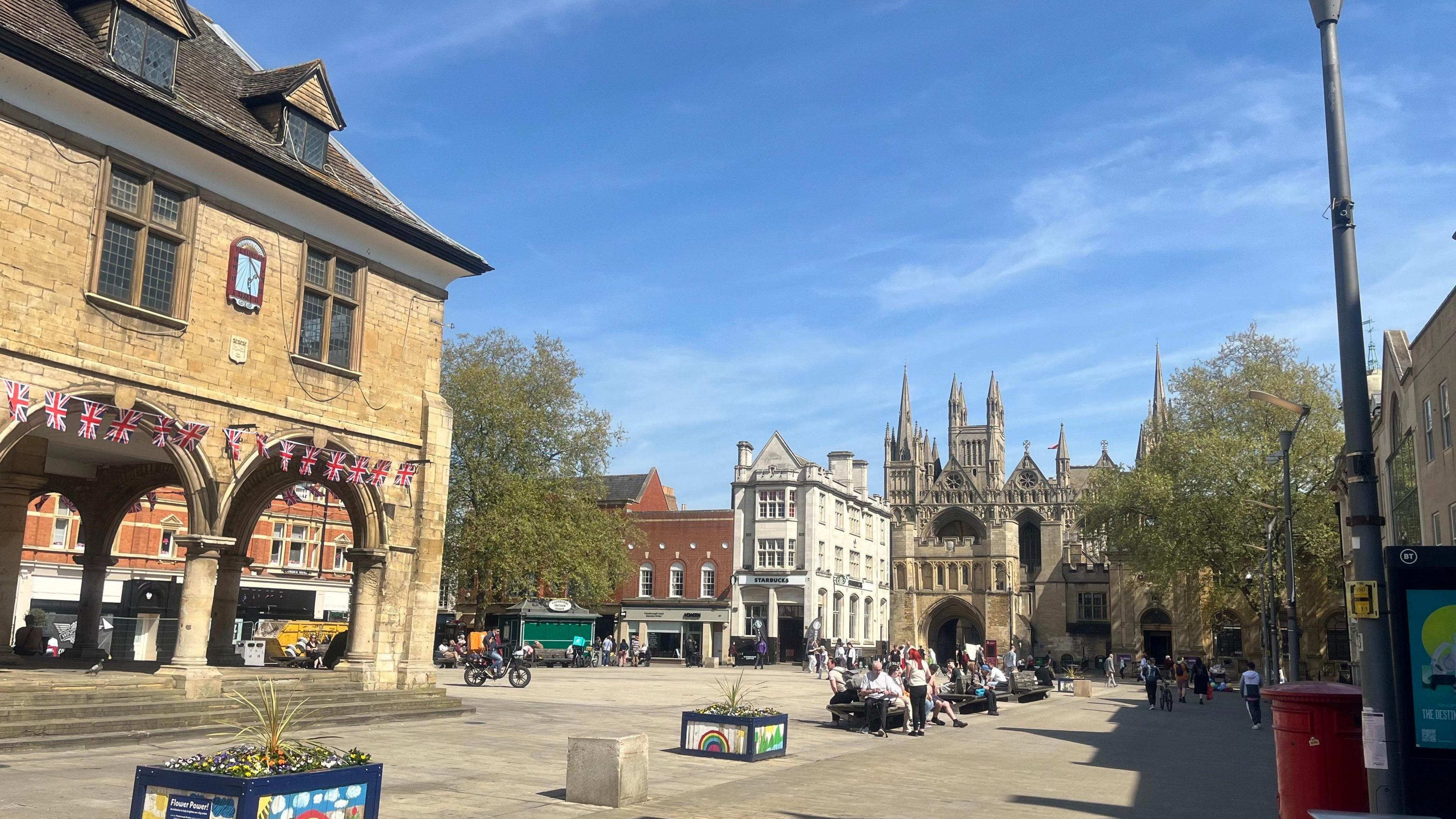 A view of the centre of Peterborough showing the cathedral in the background and people sitting in a paved square