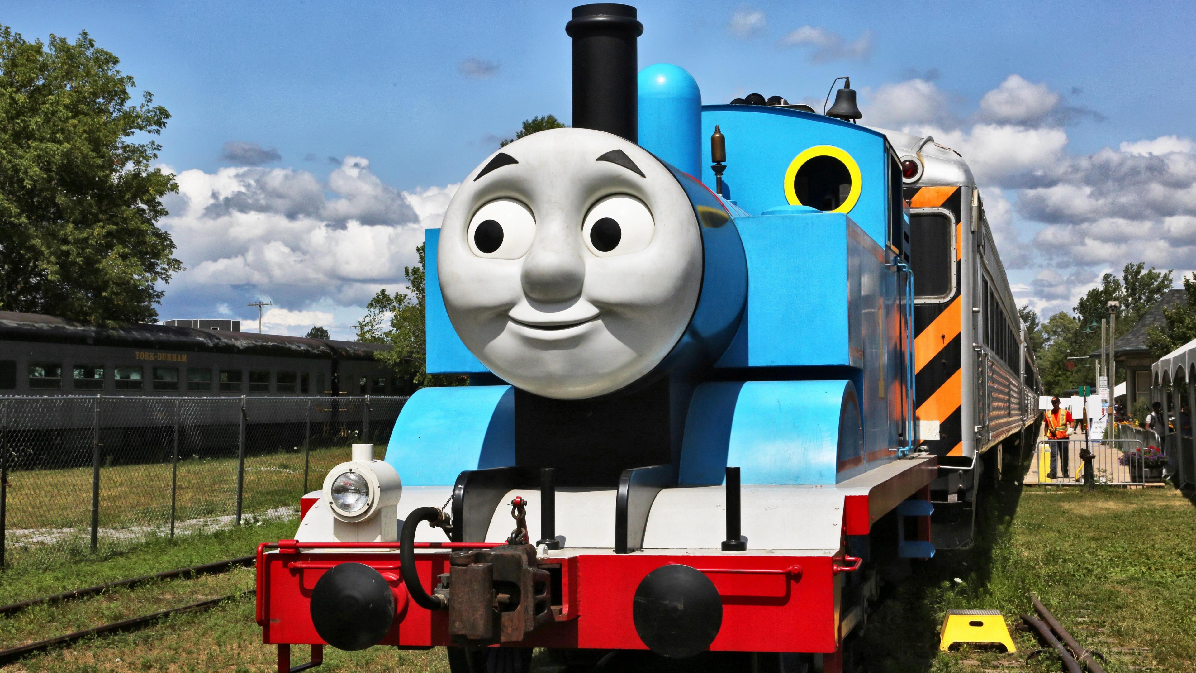 A replica of Thomas the Tank Engine. It is a blue model steam train with a grey smiley face on the front.