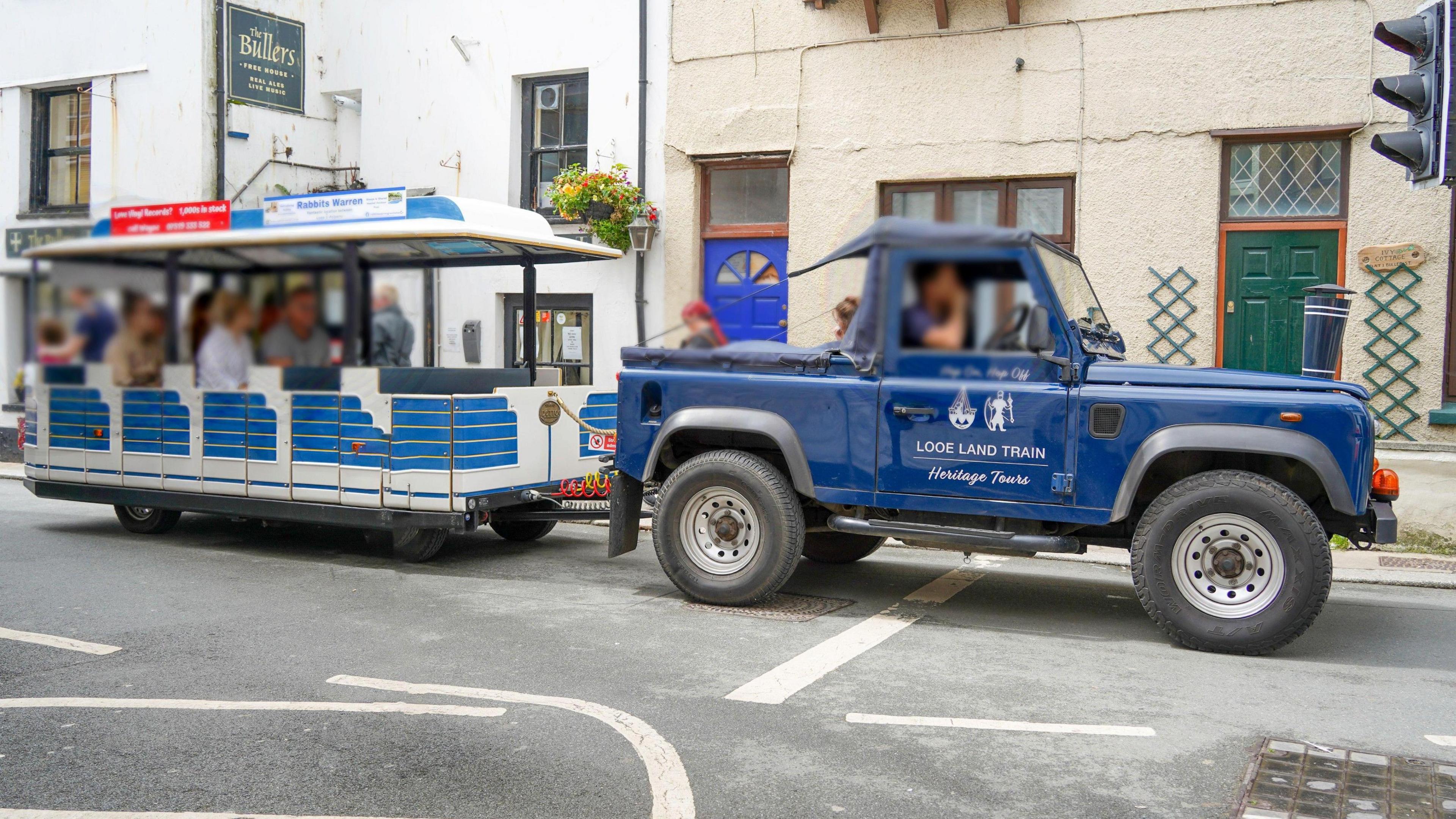 The Looe Land Train with a blue Land Rover Defender carrying a trailer with people in the back.