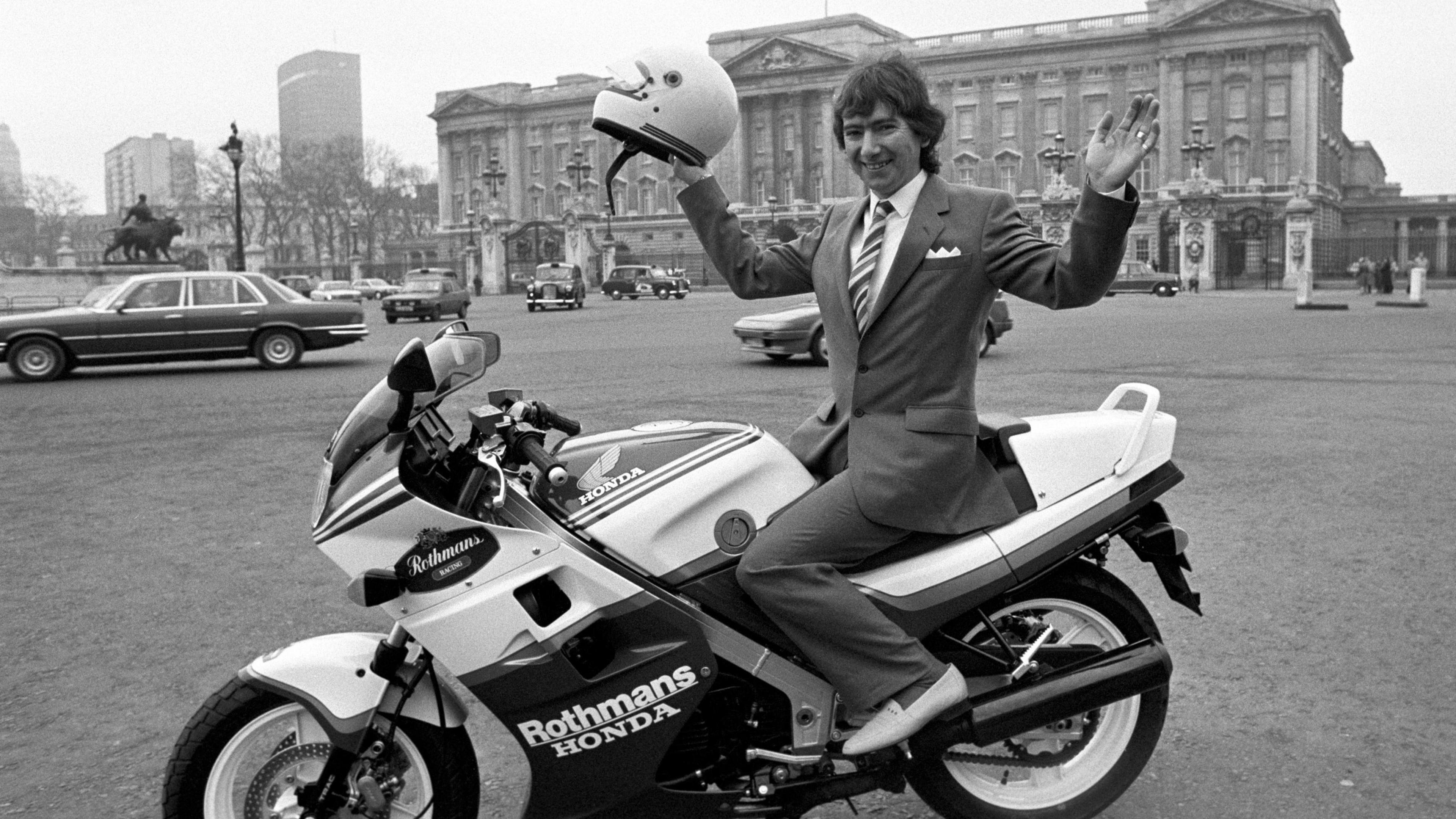 Joey Dunlop, pictured in 1986, holds a helmet aloft while on top of a Honda bike outside Buckingham Palace
