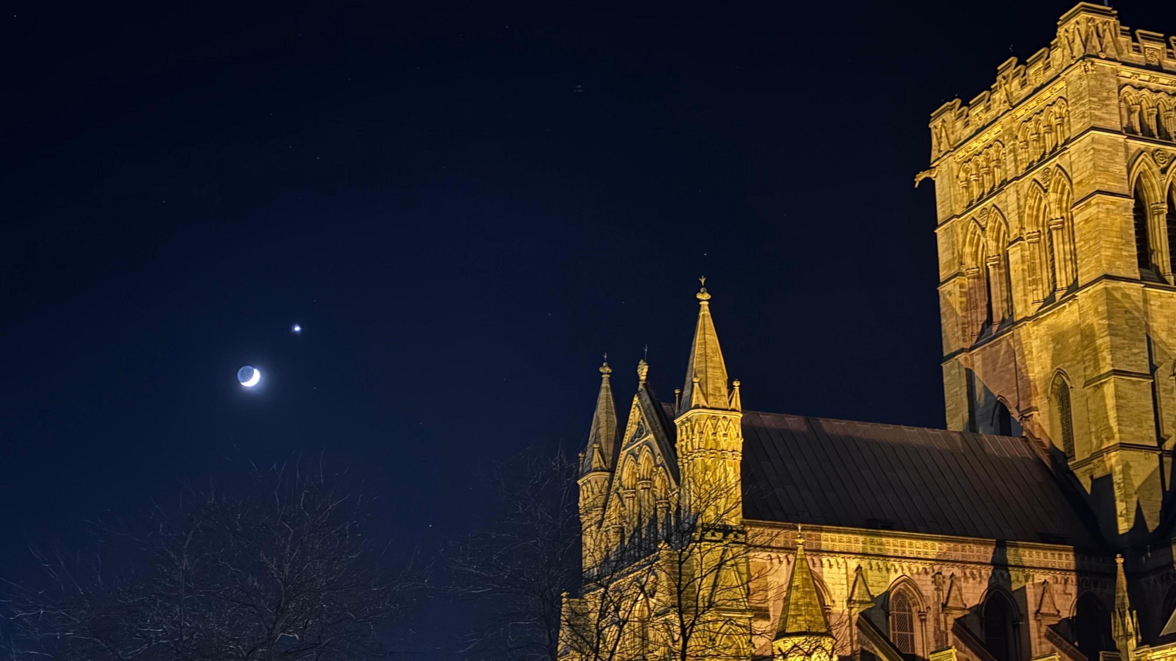 The Roman Catholic Cathedral of St John the Baptist is outshone by Venus and the moon. The building is uplit with a warm beam. 